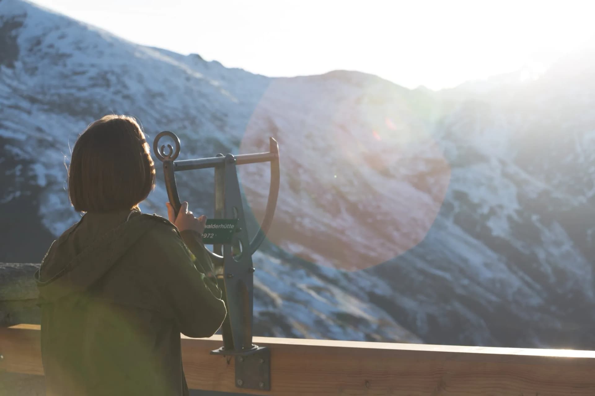 Woman looking through coin-operated viewer at snow-dusted mountain from Edelweissspitze viewpoint