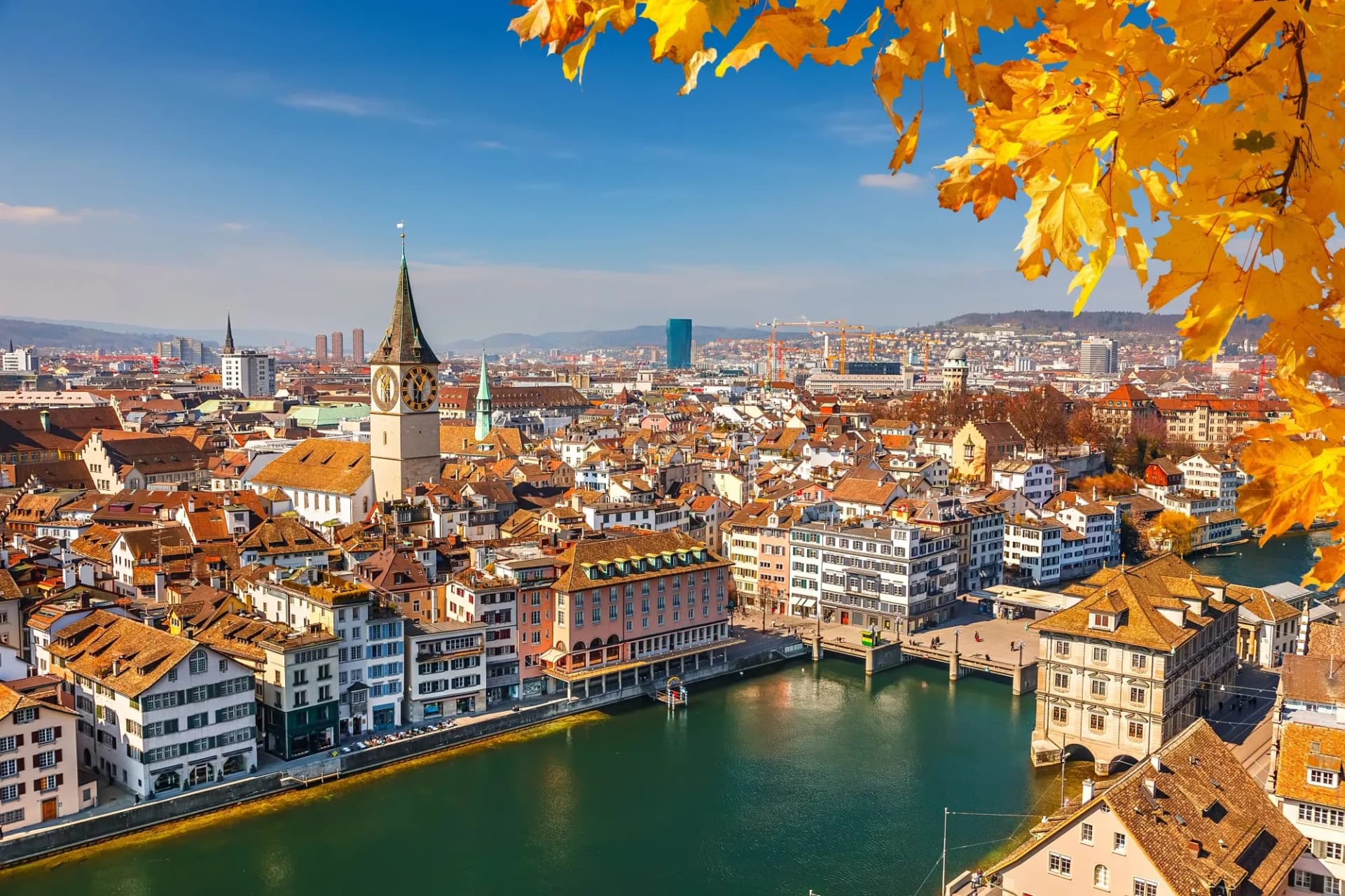 Zurich cityscape with river, clock tower, and autumn leaves overhead