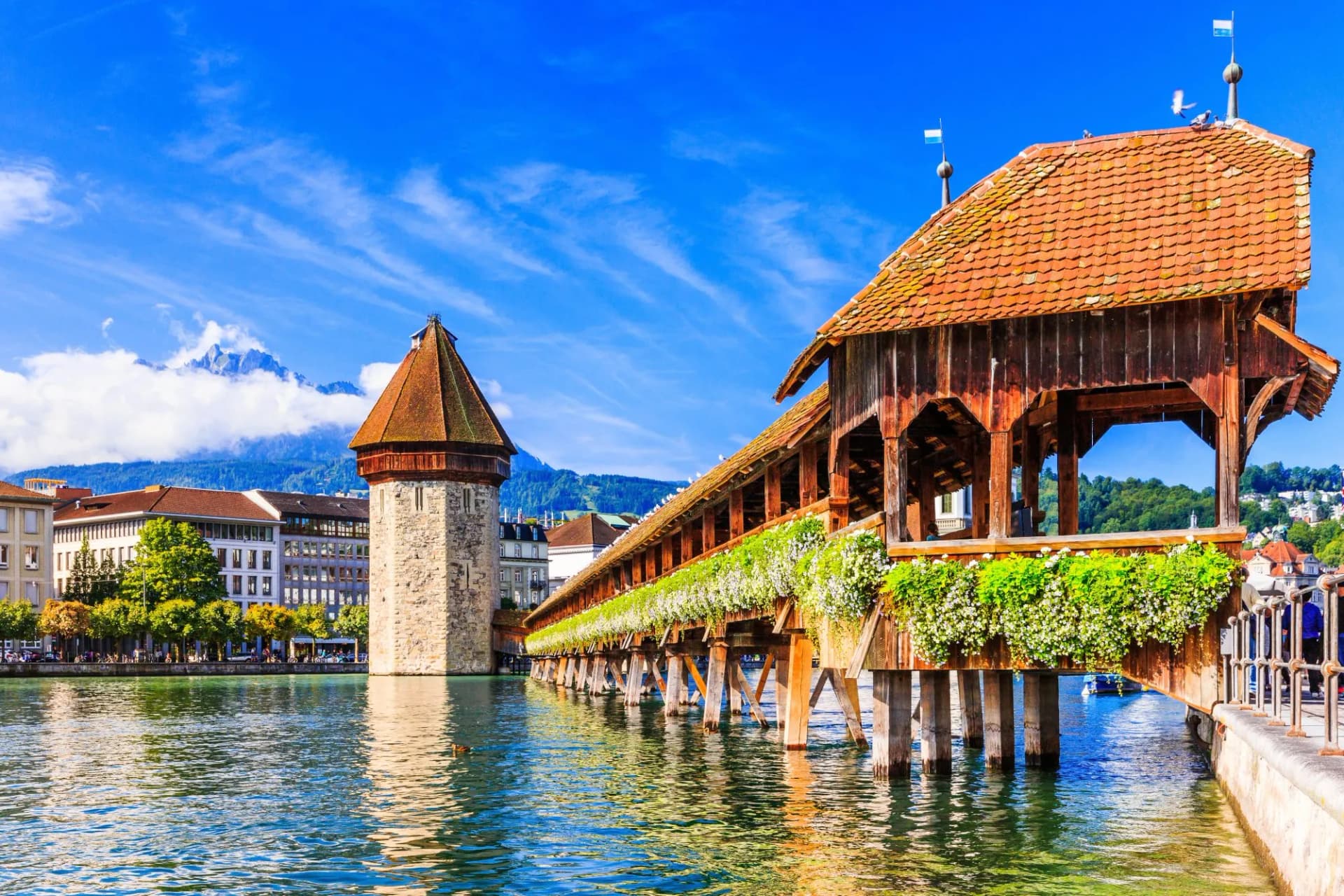 Chapel Bridge and Water Tower over river in Lucerne, Switzerland with mountain backdrop.