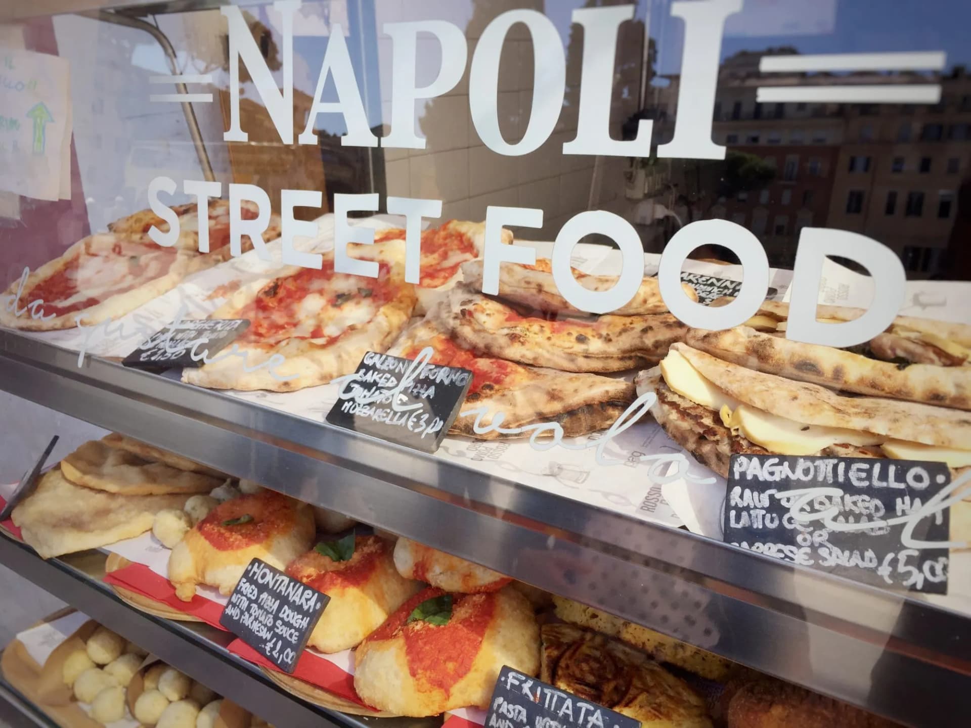 Neapolitan street food display case with pizza slices and fried dough items in Naples.