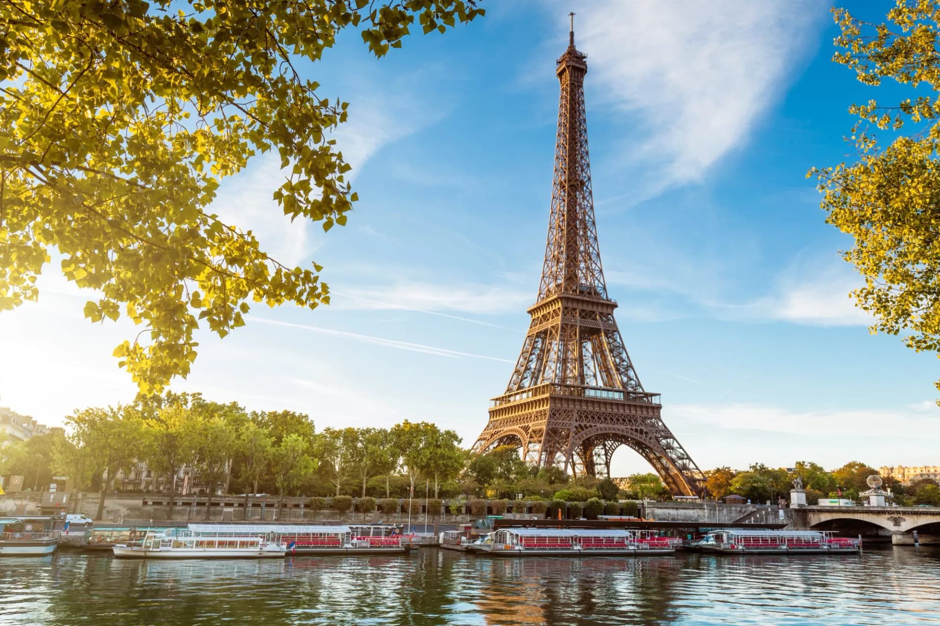 Eiffel Tower in Paris with tour boats docked on the Seine River under sunny skies.