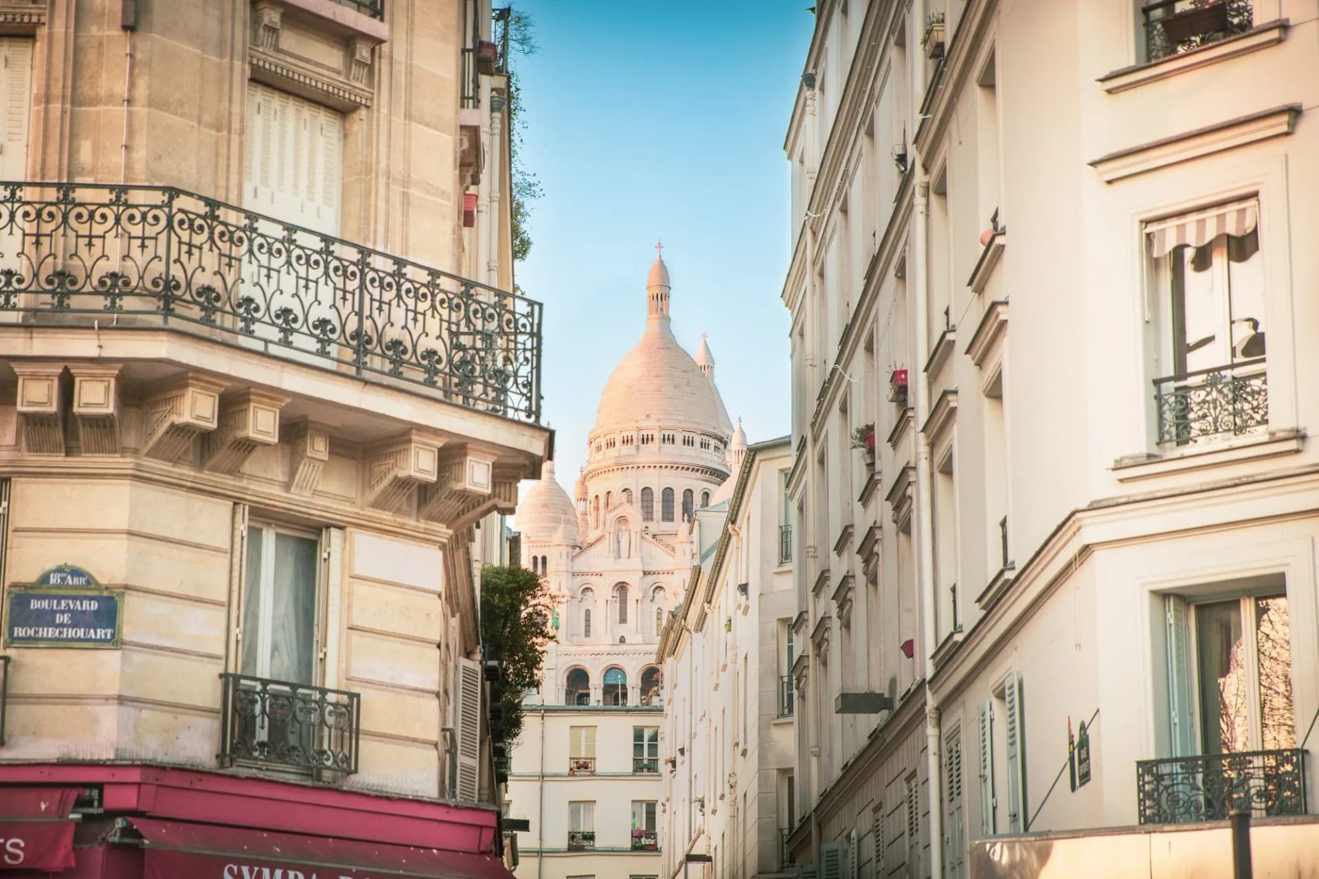 Sacre-Coeur Basilica dome visible between Parisian buildings on Boulevard de Rochechouart