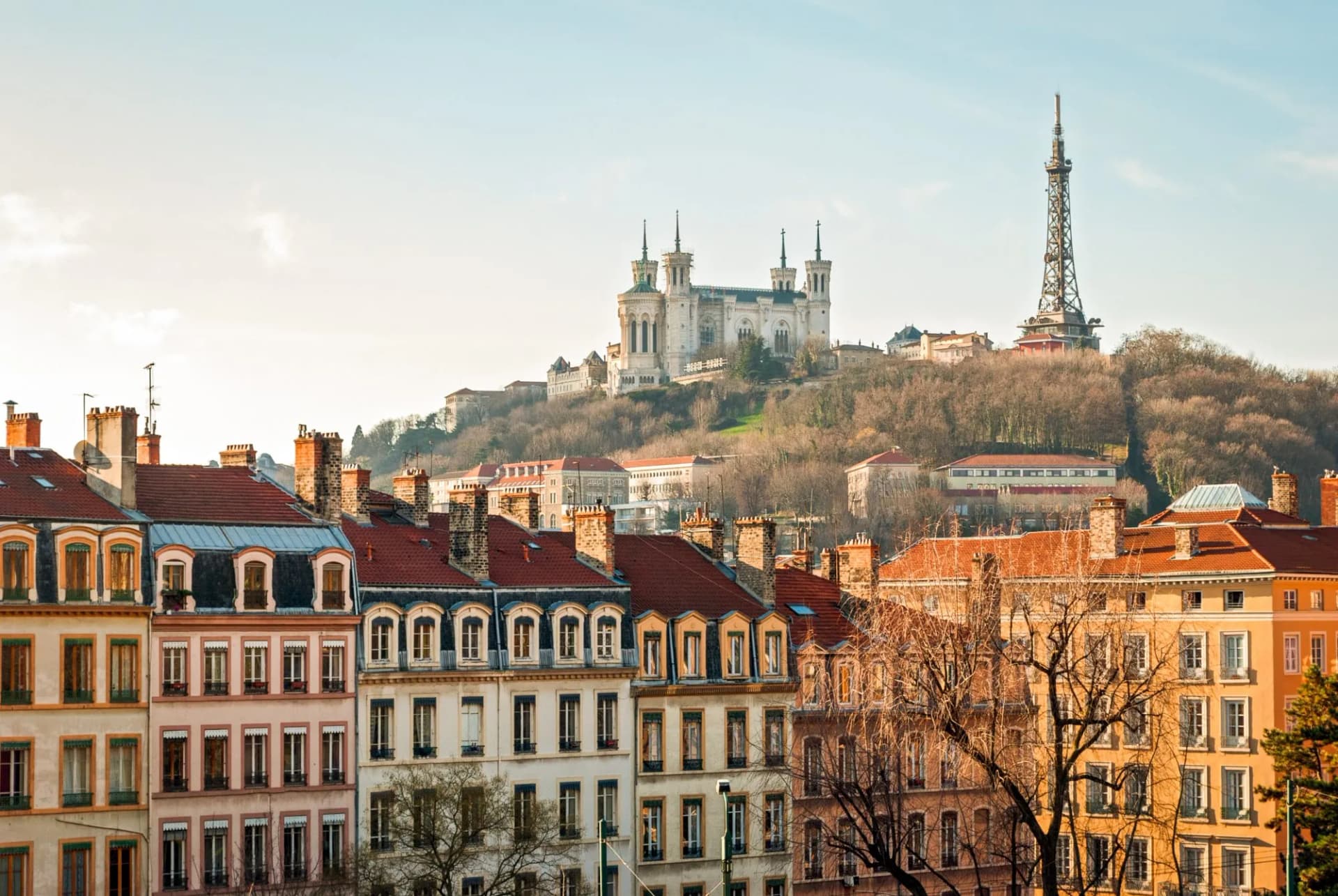 Rooftops of Lyon buildings with Basilica of Notre-Dame de Fourvière and TV tower on hill.