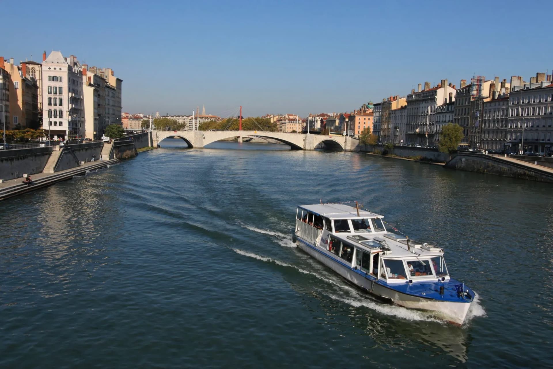 Tour boat cruising on the Saône river past historic buildings and a stone bridge.