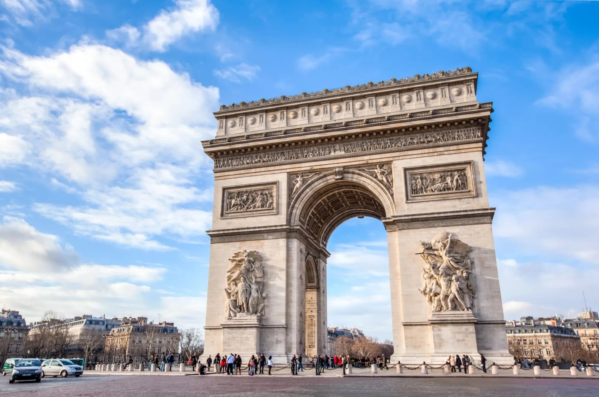 Arc de Triomphe monument in Paris under a bright blue sky with scattered clouds.
