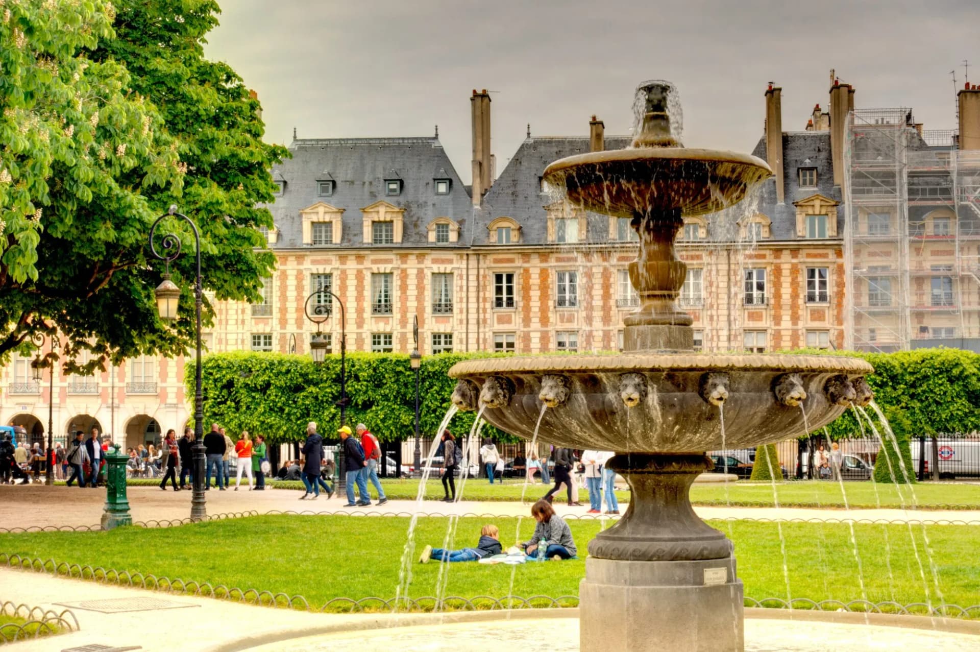 Stone fountain in green park with people walking, Place des Vosges, Paris.