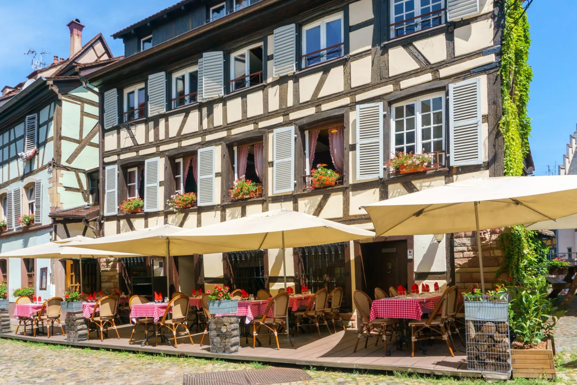 Outdoor restaurant seating with half-timbered buildings and red checkered tablecloths in Strasbourg.