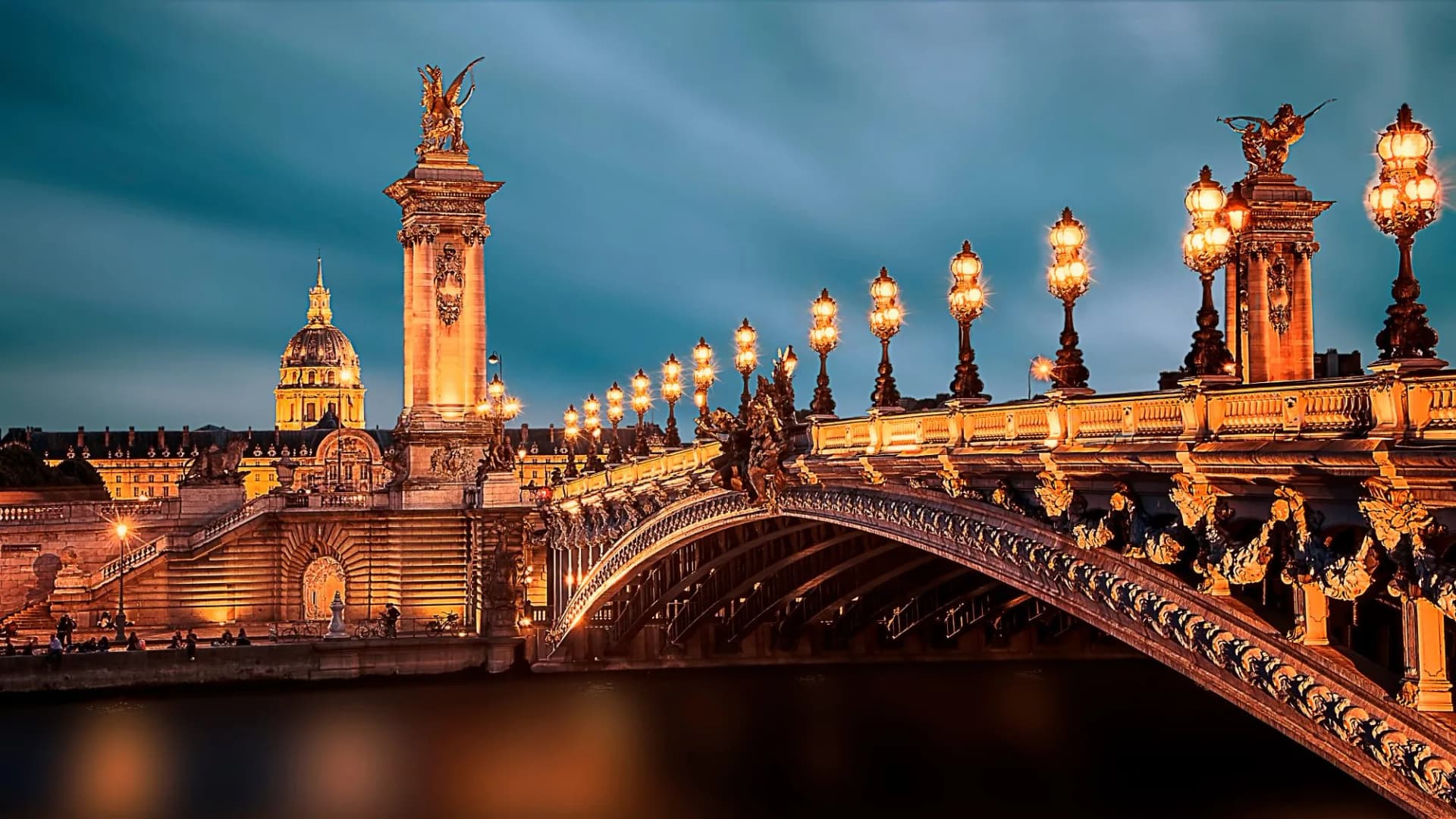 Pont Alexandre III bridge illuminated at night in Paris with Les Invalides dome in background.