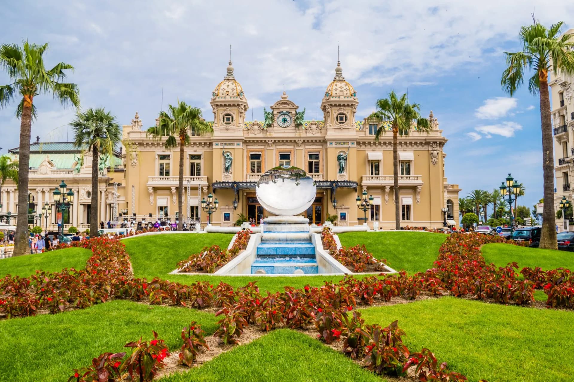 Casino de Monte-Carlo with fountain, reflective sphere, and manicured gardens with palm trees.