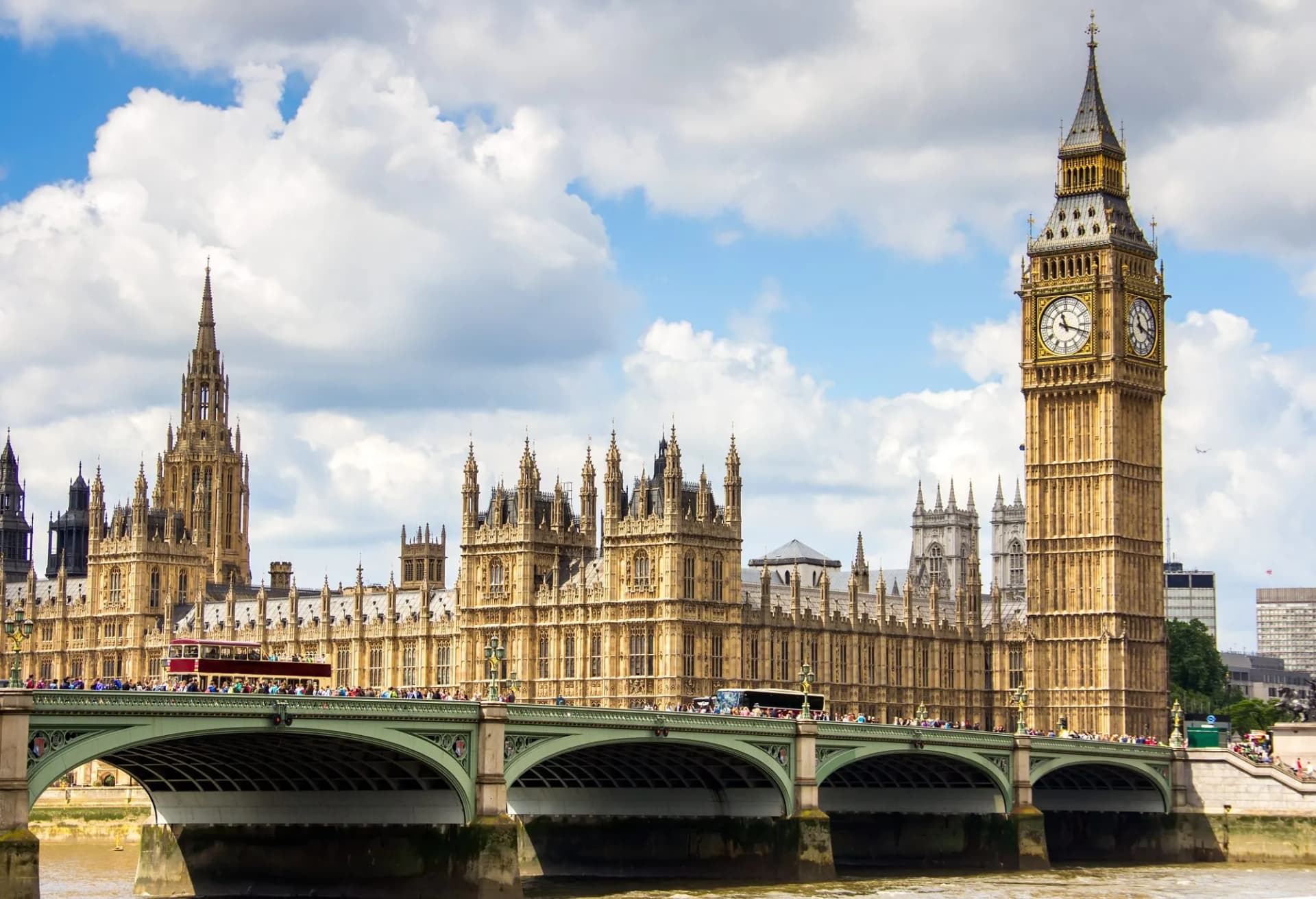 Palace of Westminster and Big Ben tower over Westminster Bridge with a red bus.