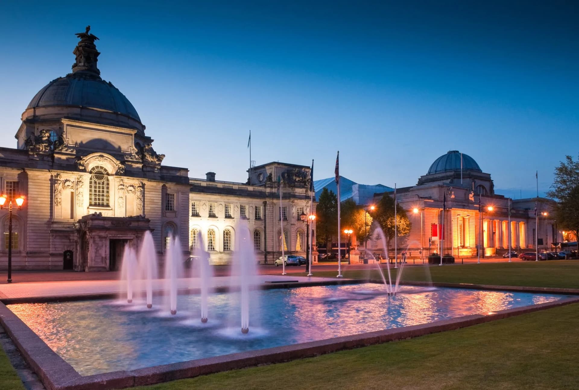 City Hall Cardiff UK illuminated at dusk with fountains operating in the foreground.