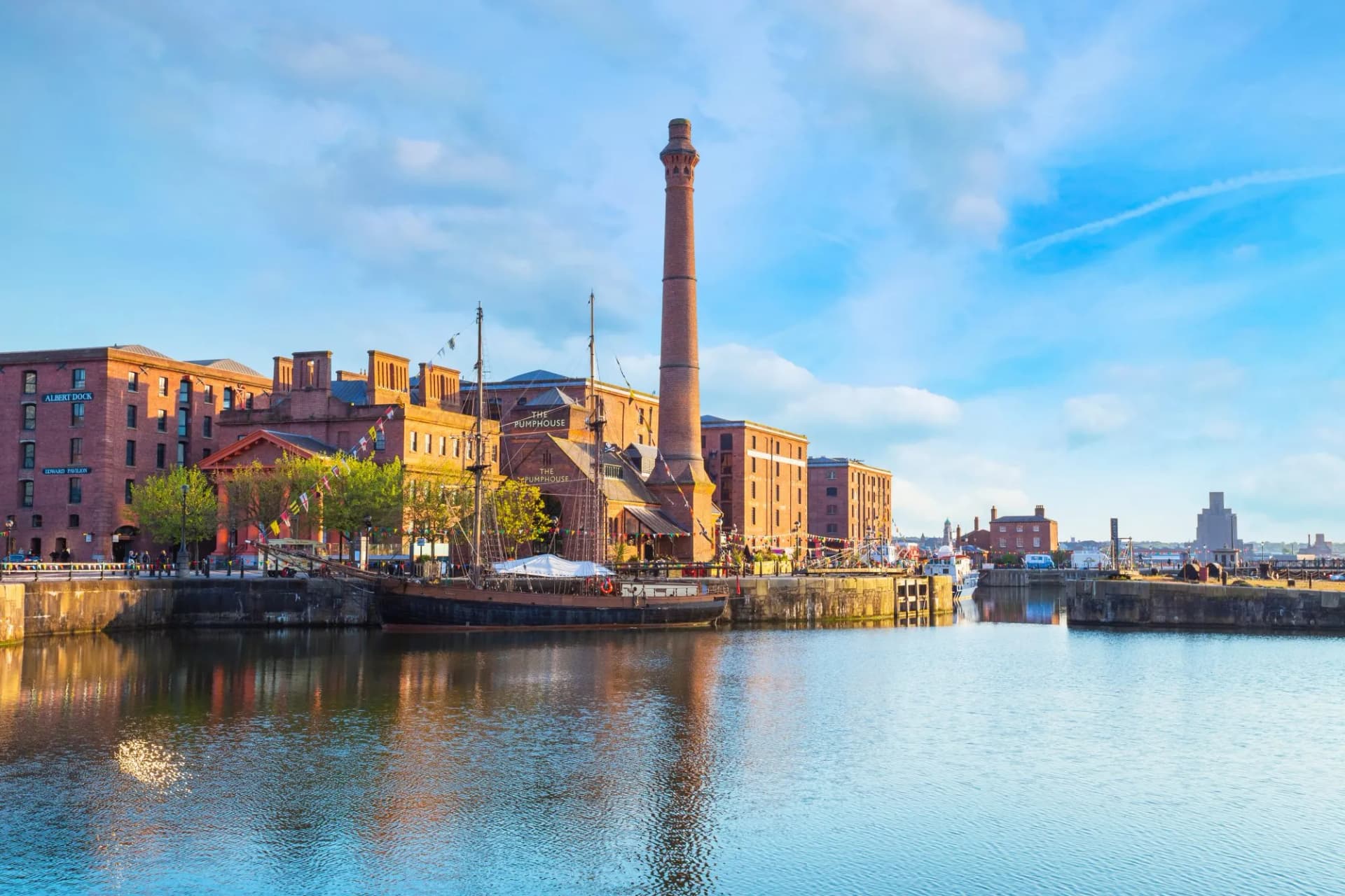 Royal Albert Dock in Liverpool with brick warehouses, a tall chimney, and a moored historic ship.