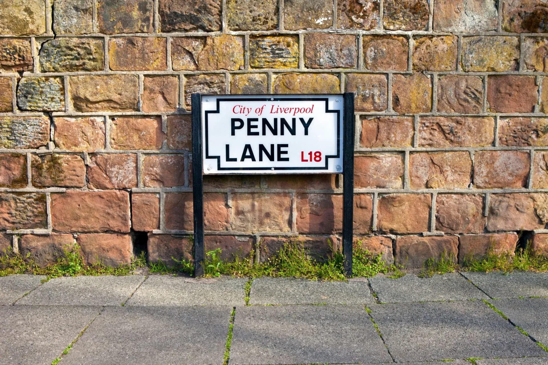 Penny Lane street sign in Liverpool mounted on a rough-cut sandstone brick wall above pavement.