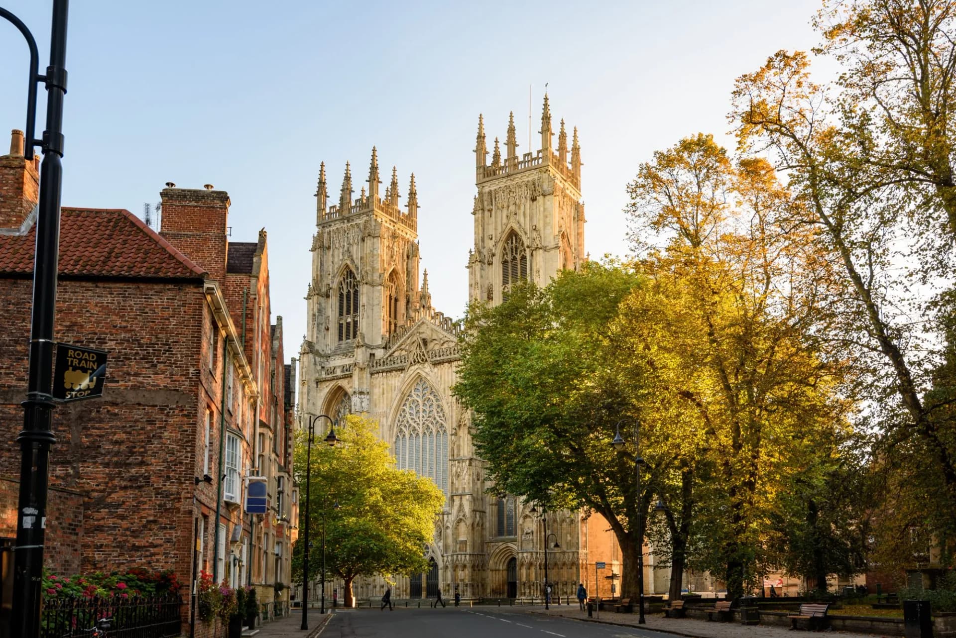 York Minster cathedral towers seen from a street with brick buildings and autumn trees in England.