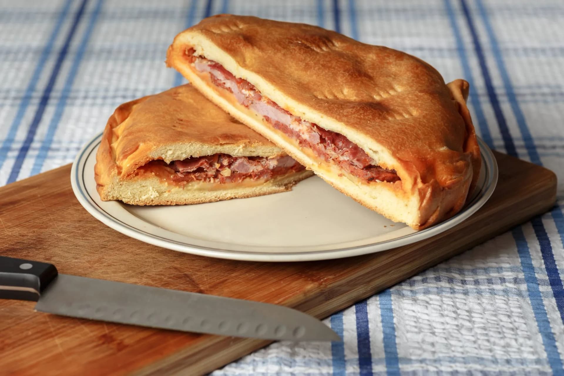 Hornazo savory stuffed bread cut in half on a plate with a knife on a cutting board.