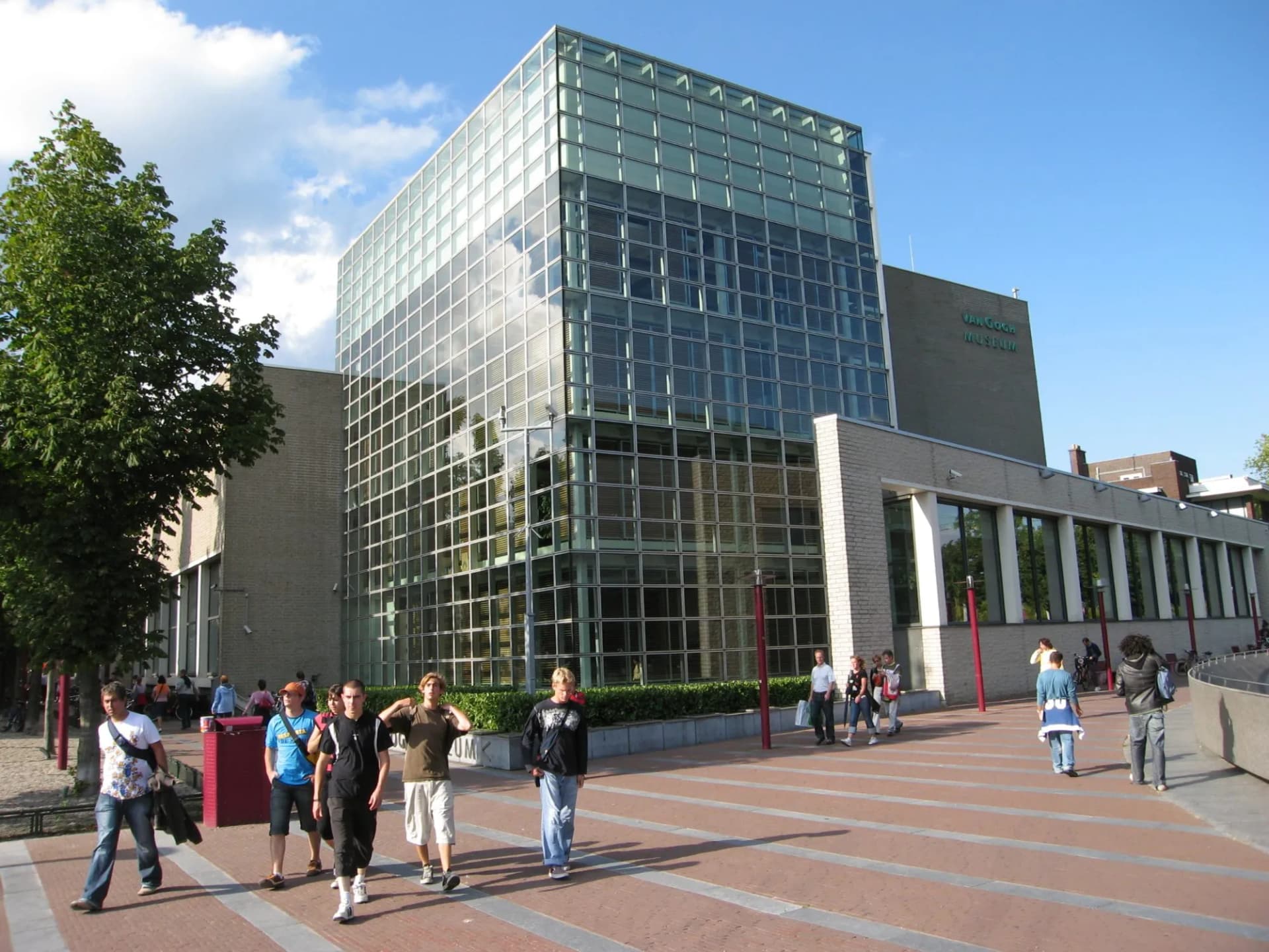 Van Gogh Museum Amsterdam building exterior with pedestrians walking on paved plaza.