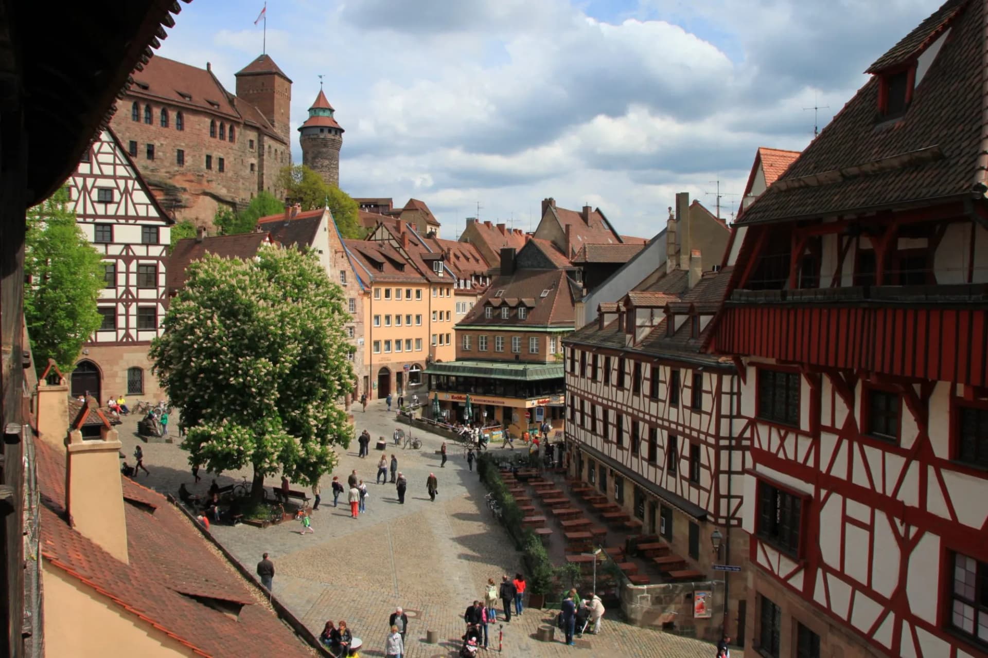 Cobblestone square with half-timbered buildings and Nuremberg Castle in the background.