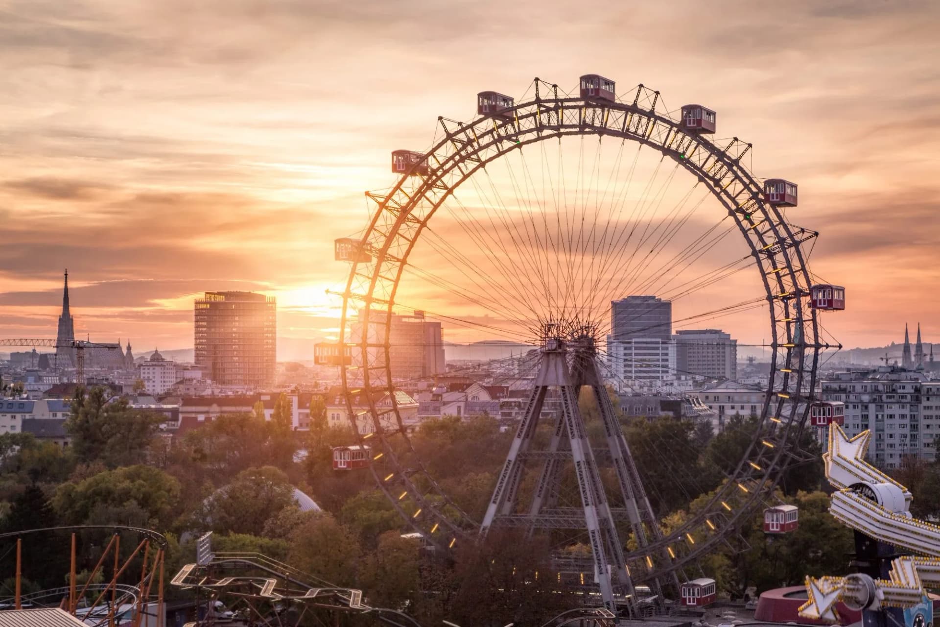 Vienna Ferris Wheel at sunset over city skyline and amusement park rides.