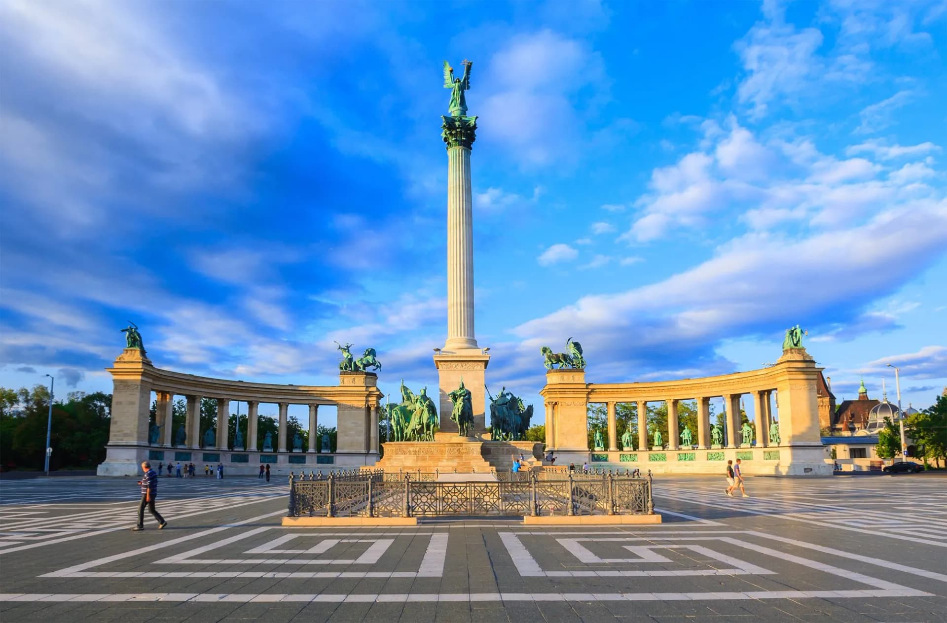 Heroes Square Budapest with central column, statues, and colonnade under a blue sky.