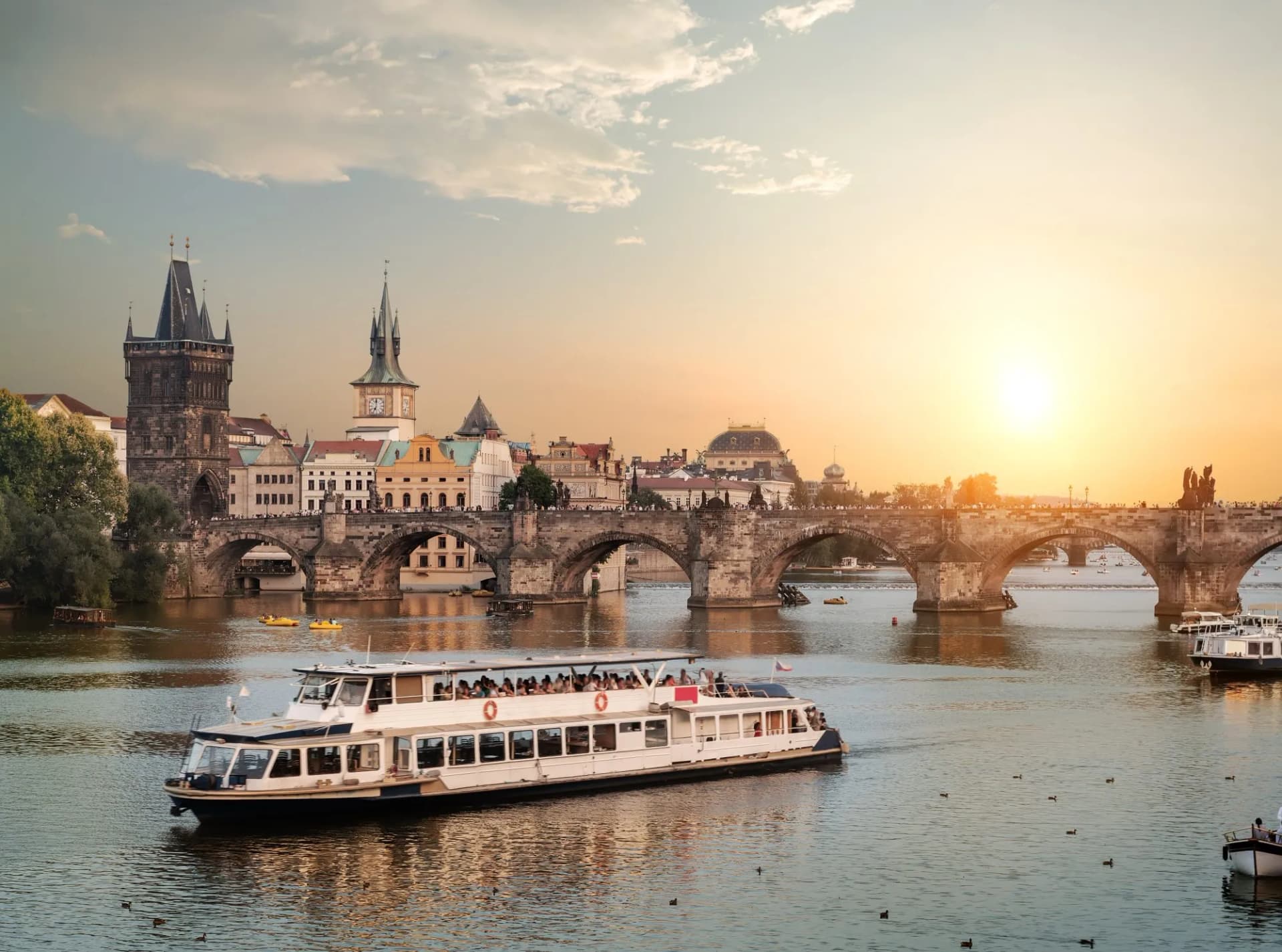 Touristic boat on river near Charles Bridge and Prague skyline at sunset