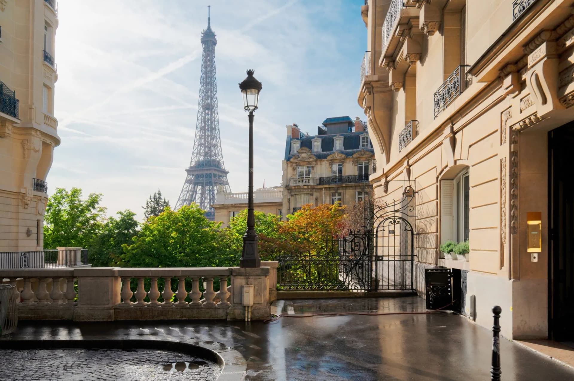 Eiffel Tower view from wet Parisian street with classic buildings and lamppost