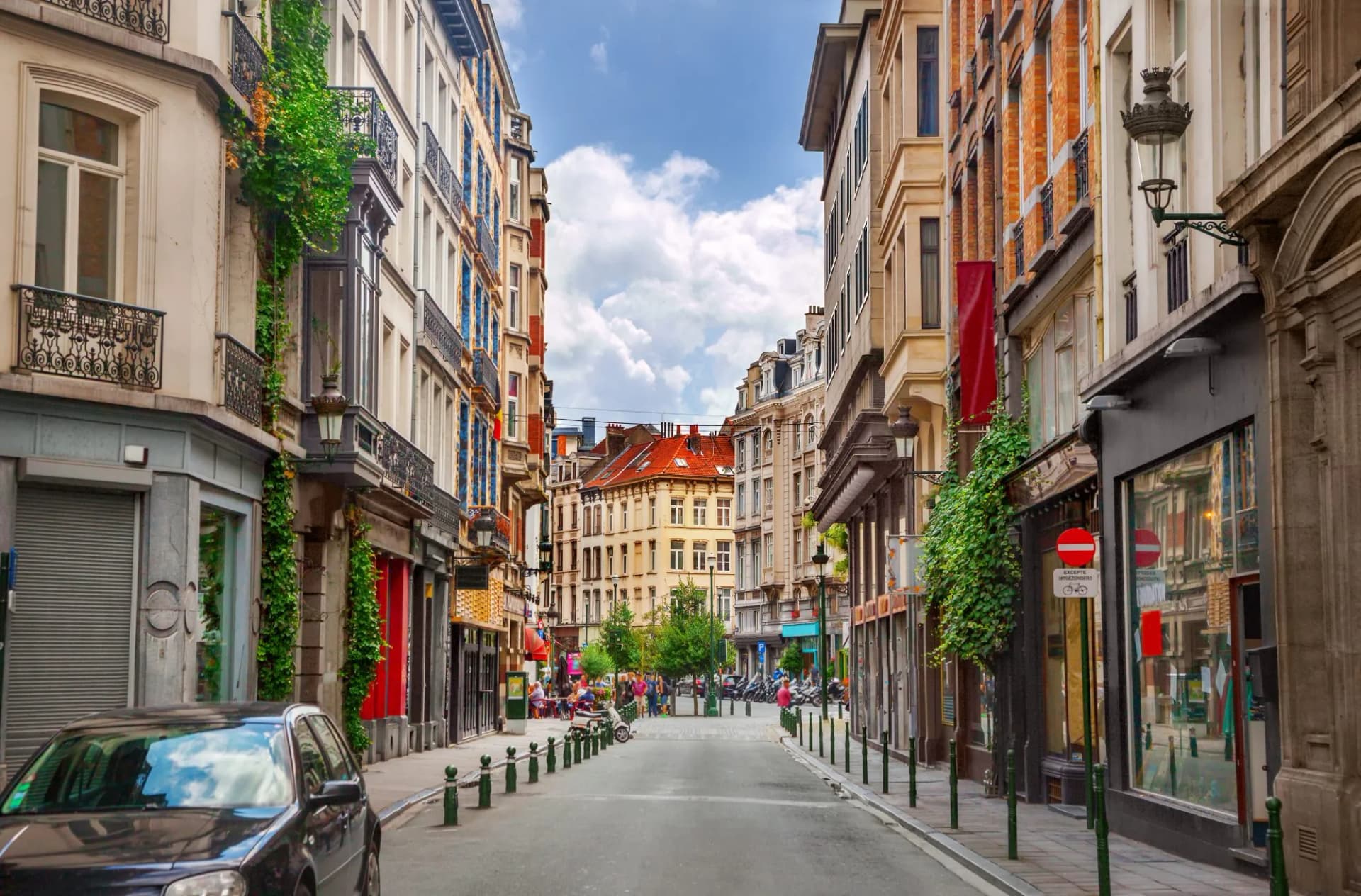 Narrow street in Brussels with historic buildings, parked car, and people in the distance.