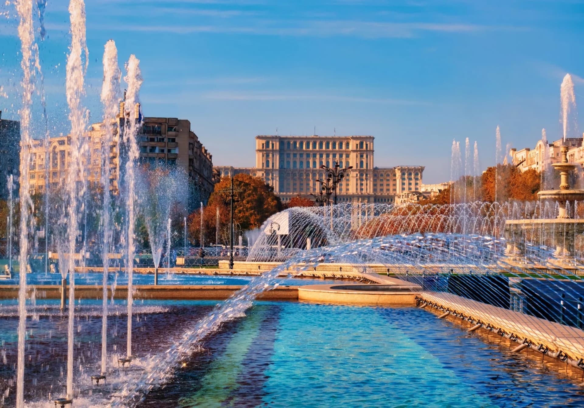 Fountains spraying water in foreground with Palace of the Parliament in Bucharest background.