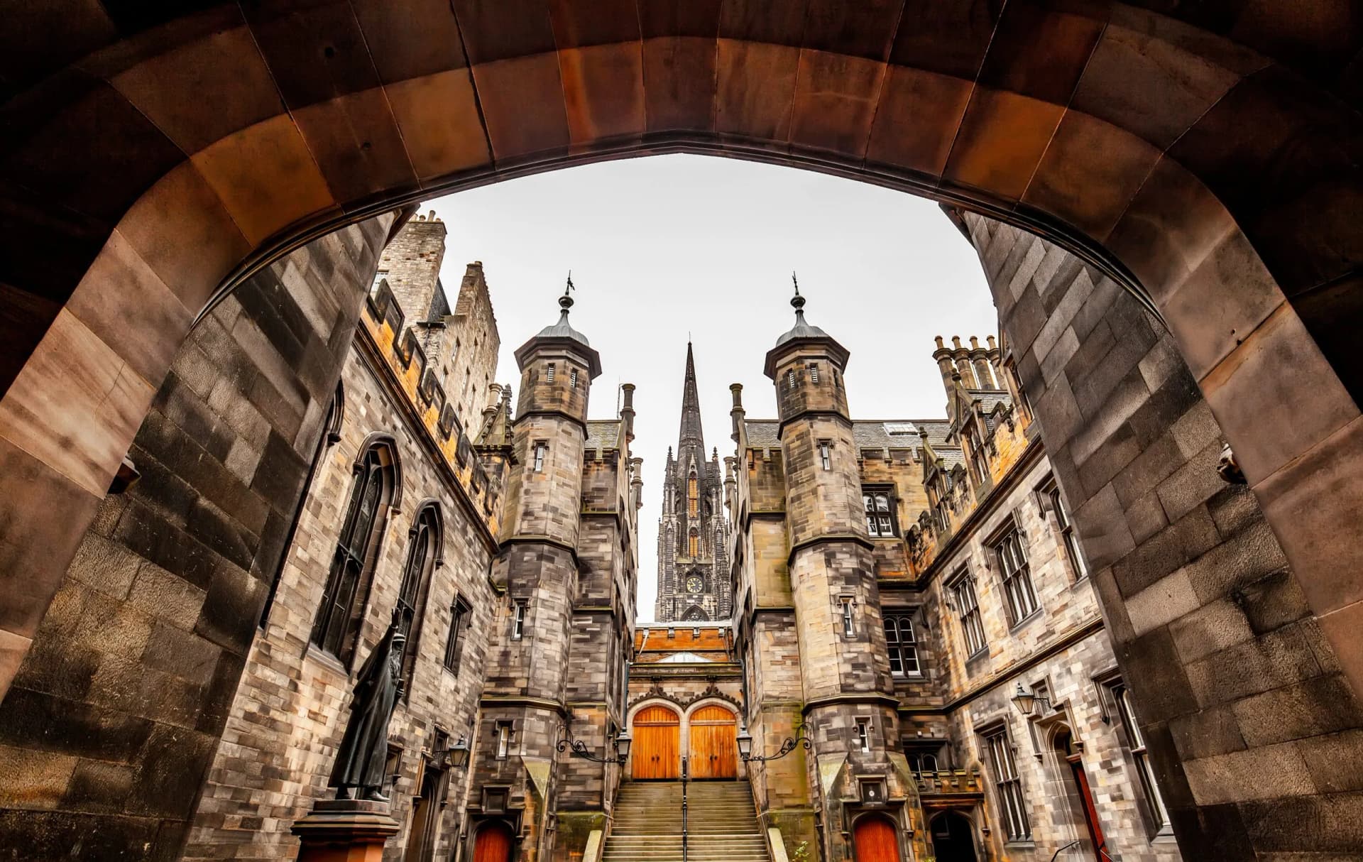 Historic stone architecture framed by an archway in Edinburgh Old Town, with a spire visible.