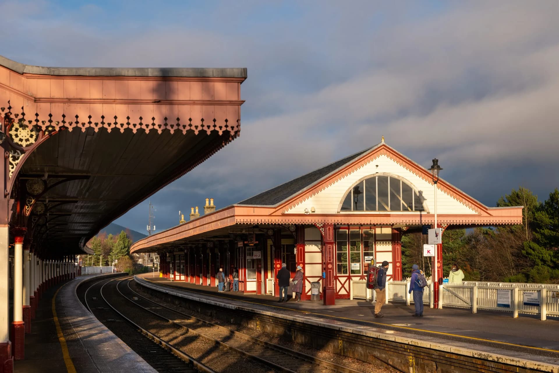 Victorian railway station platform with ornate trim, tracks curving, and mountains in Aviemore, Highlands, Scotland.