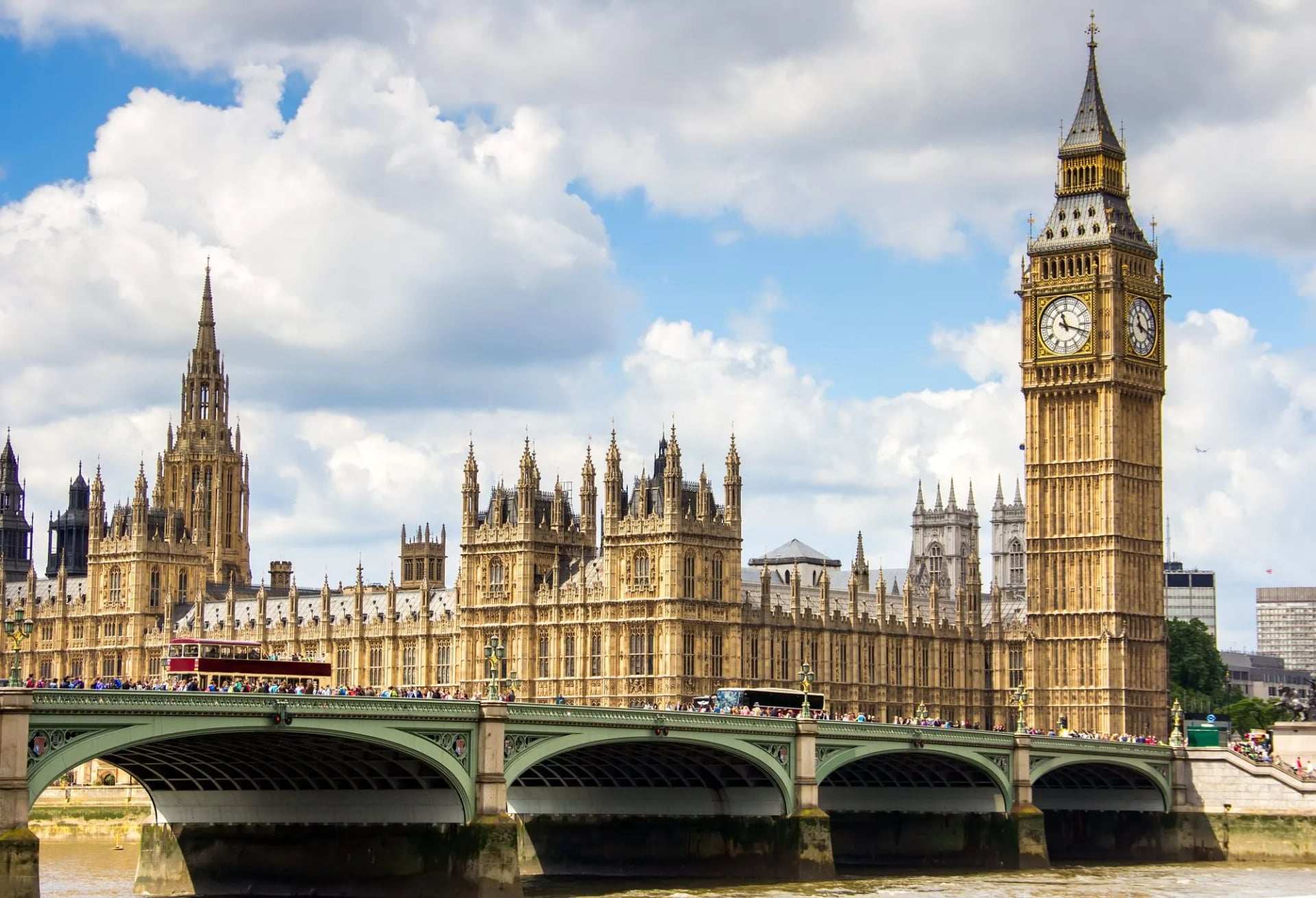 Palace of Westminster and Big Ben tower over Westminster Bridge with a red bus.