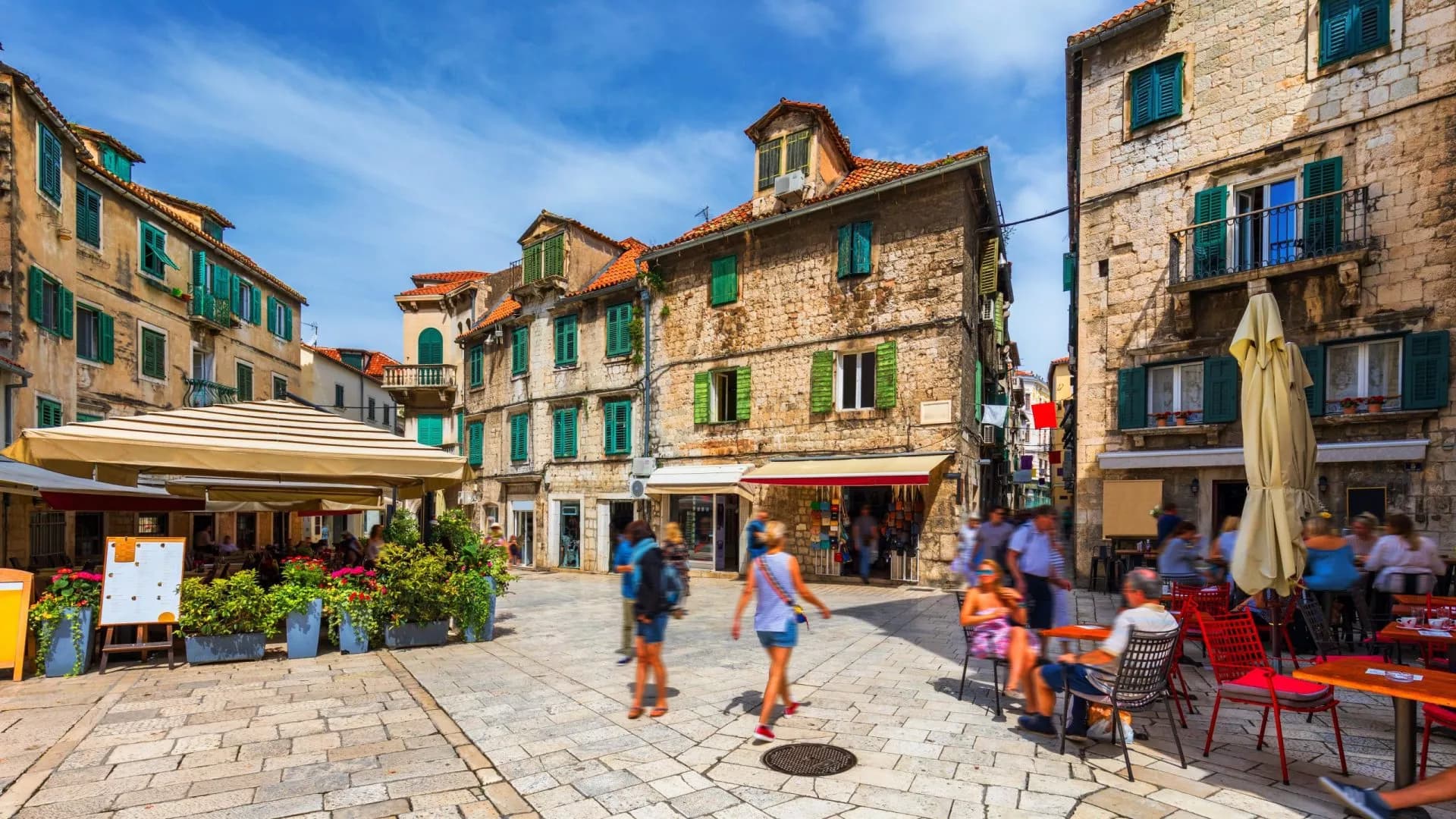 Old stone street in Split historic center, Croatia, with outdoor cafe seating under a striped awning.