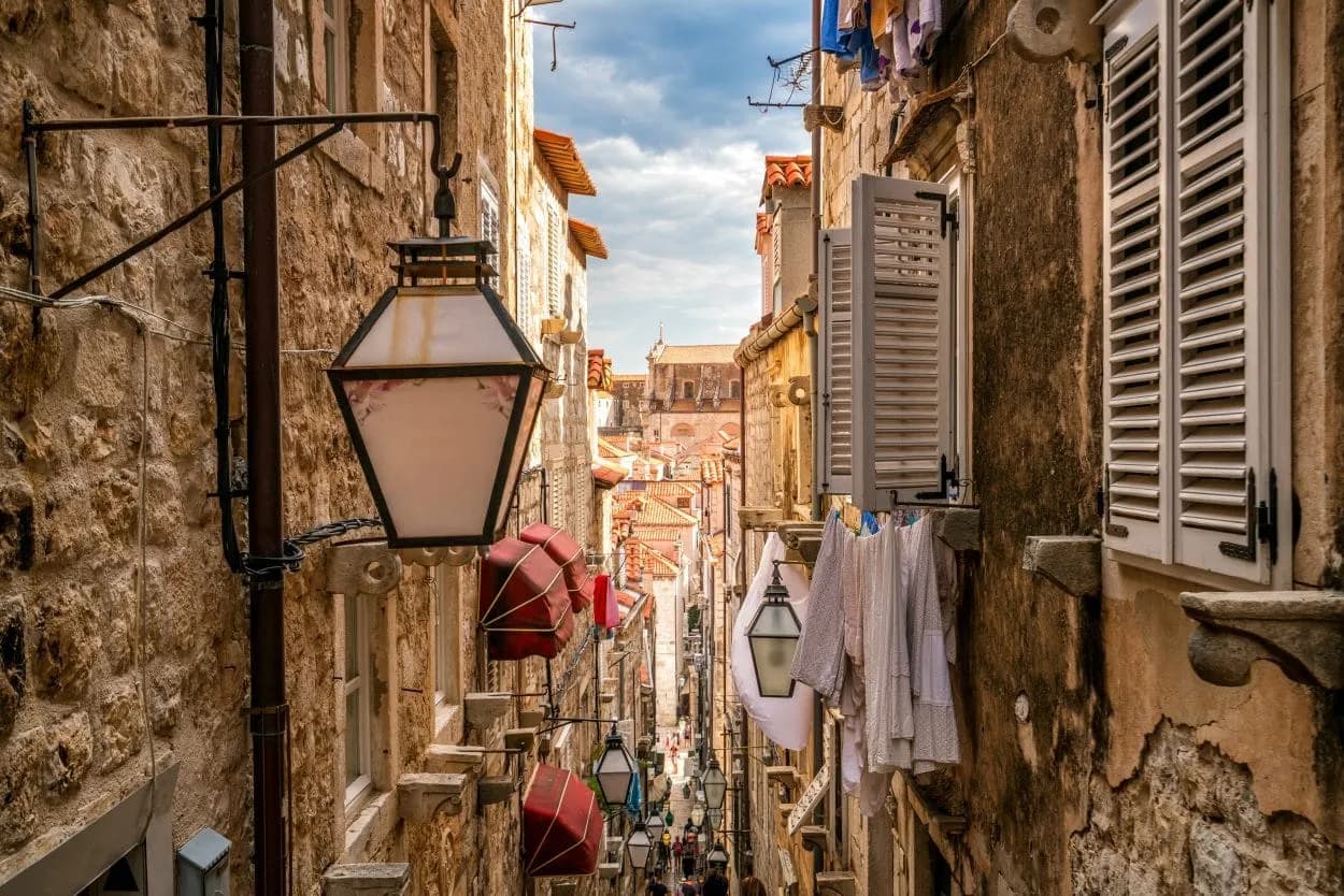 Narrow Dubrovnik street with stone buildings, hanging lanterns, and laundry drying outdoors