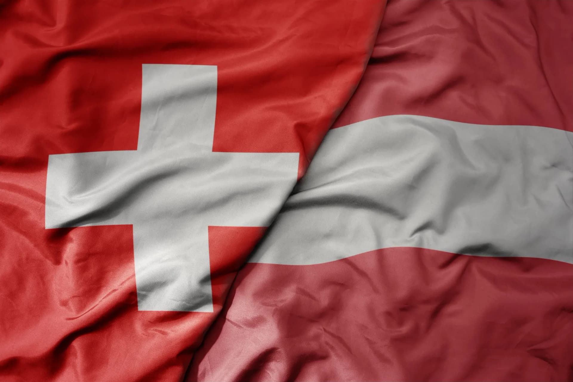 Waving fabric featuring the national flag of Switzerland next to the national flag of Austria.