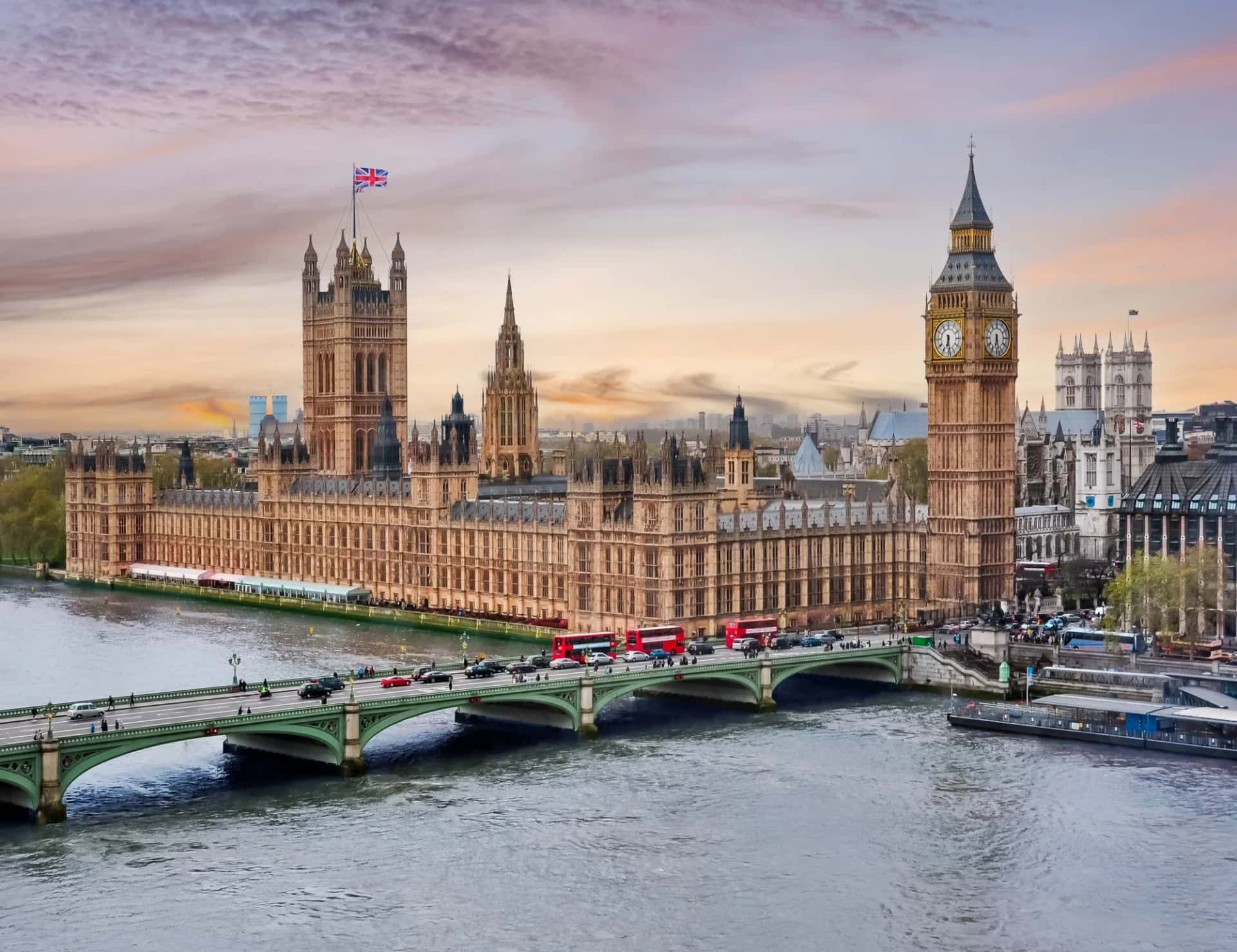 Houses of Parliament and Big Ben tower over River Thames at sunset in London, UK.