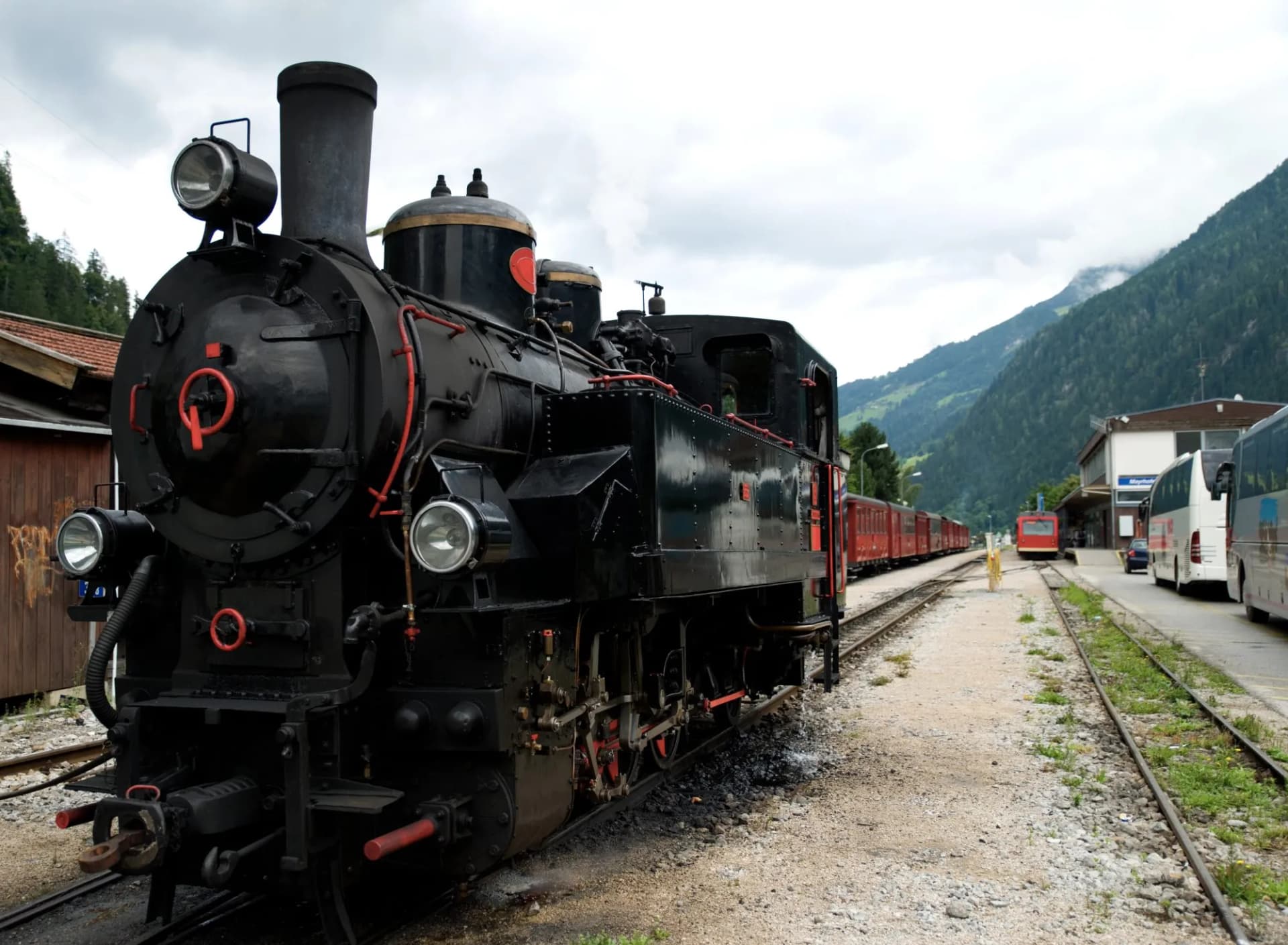 Black Zillertalbahn steam locomotive at a station with green alpine mountains in Austria.
