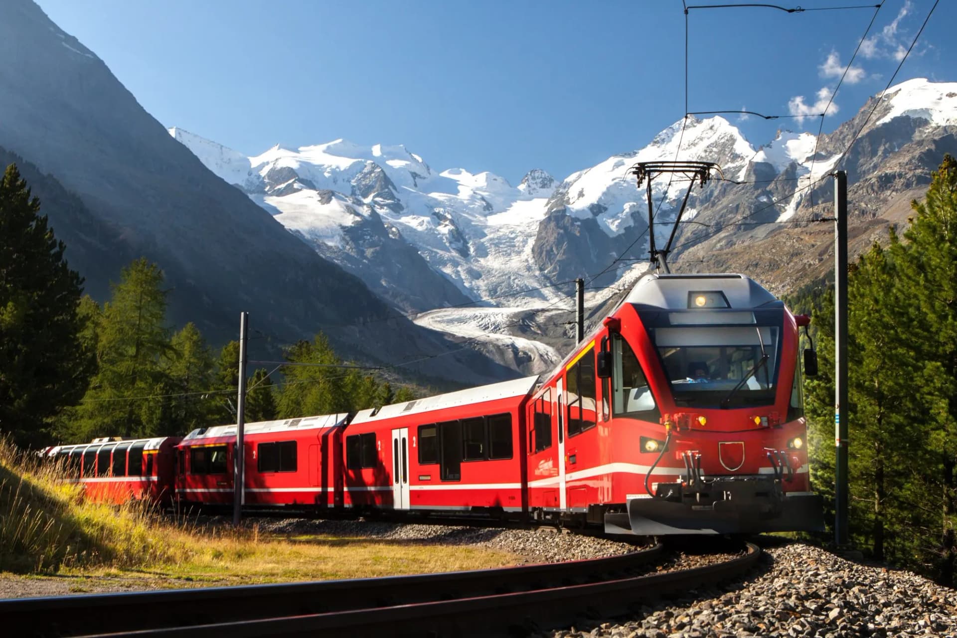 Red Bernina train traveling near Morteratsch Glacier with snow-capped mountains in Switzerland.