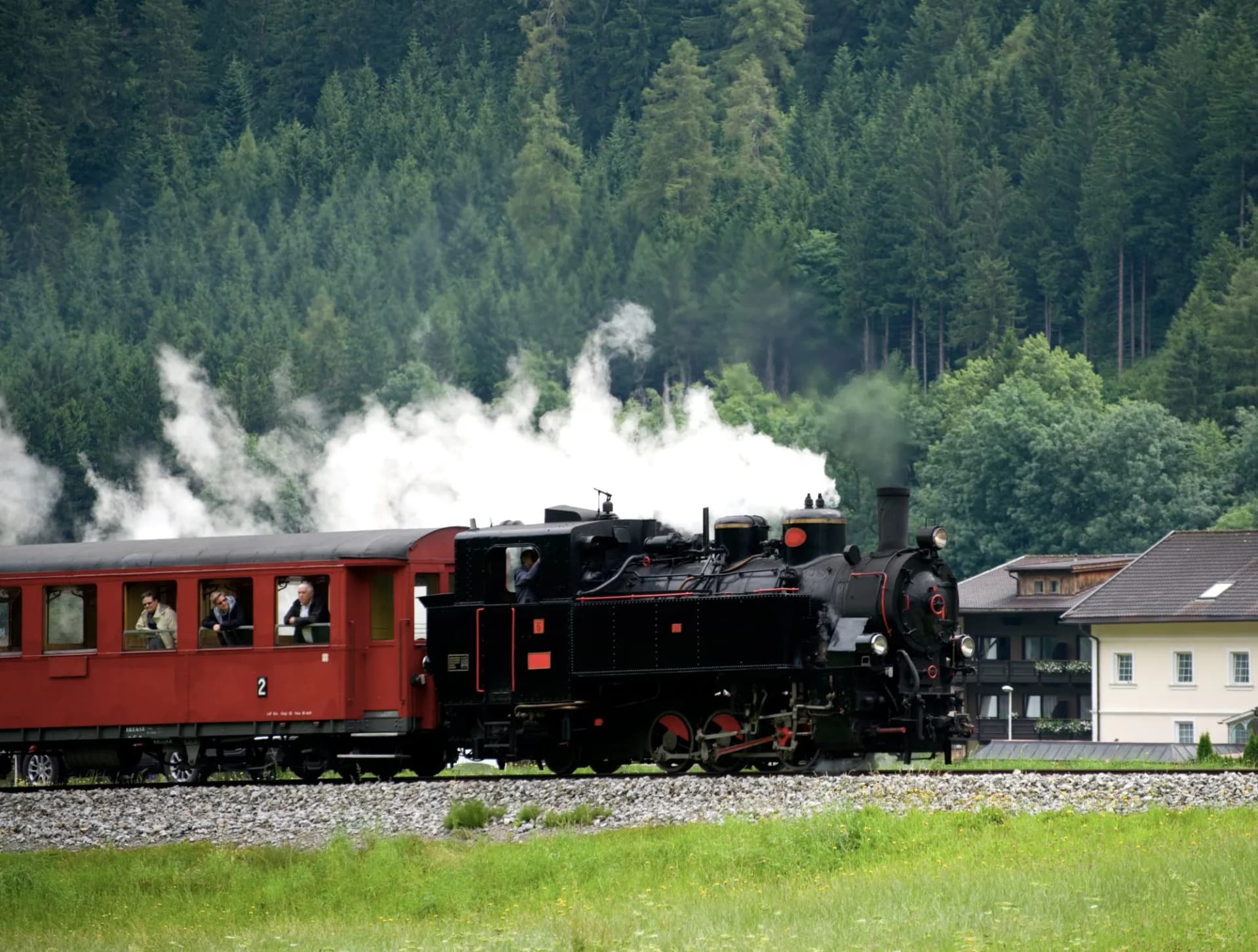 Zillertalbahn steam train with red passenger car traveling past forest and buildings in Austria.