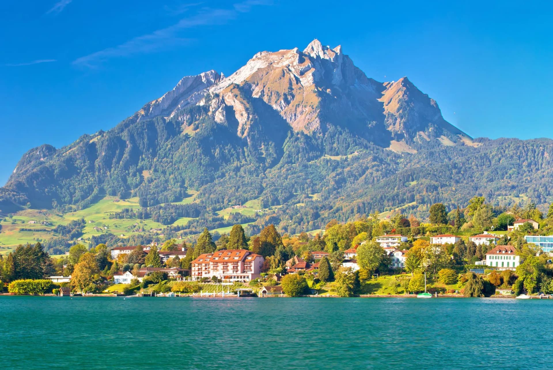 Coast of Lake Lucerne and Pilatus Mountain with lakeside village and clear blue sky.