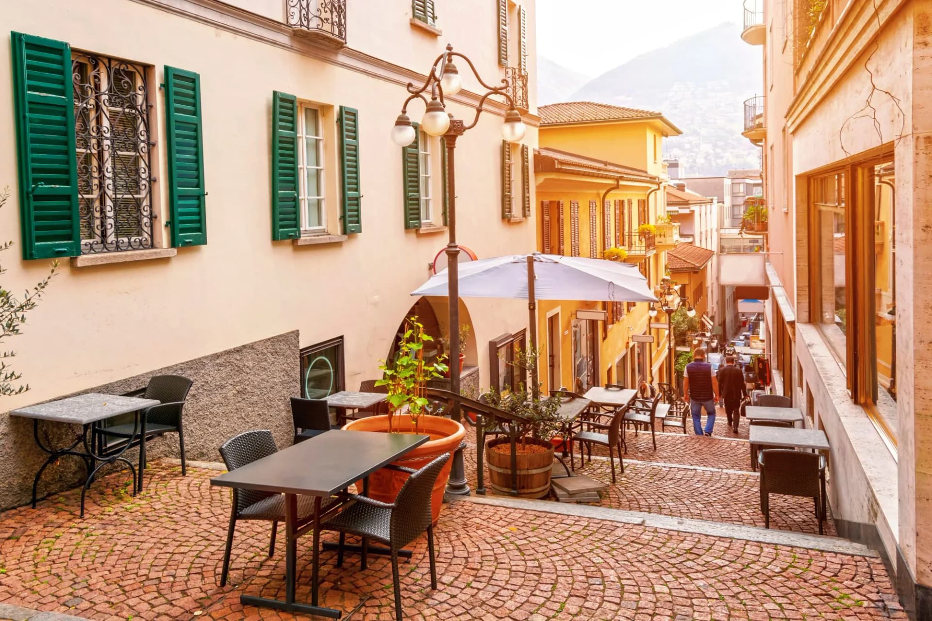 Outdoor cafe seating on a steep cobblestone street in the old town of Lugano, Ticino, Switzerland.