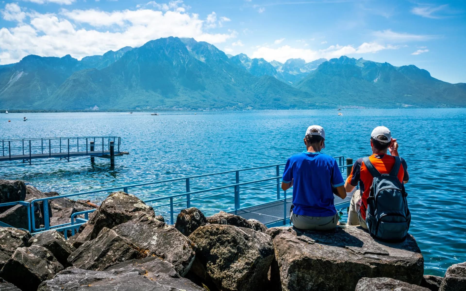 Two tourists admiring the view of Lake Geneva and the Alps from Montreux shoreline, Switzerland.