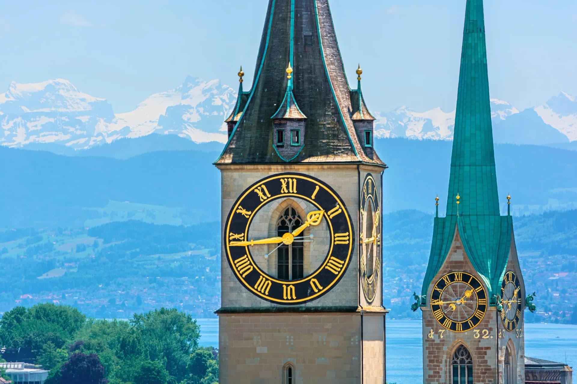 Saint Peter and Fraumünster church towers in Zurich, Switzerland, with Lake Zurich and snowy Alps.