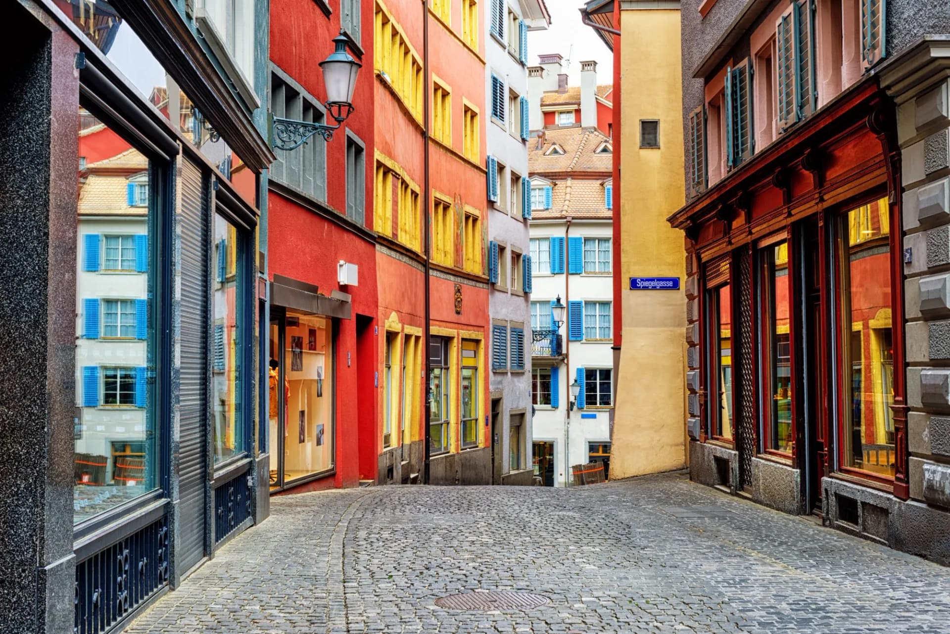 Colorful buildings line a cobblestone street in Zurich's city center, Switzerland, with a Spiegelgasse sign visible.