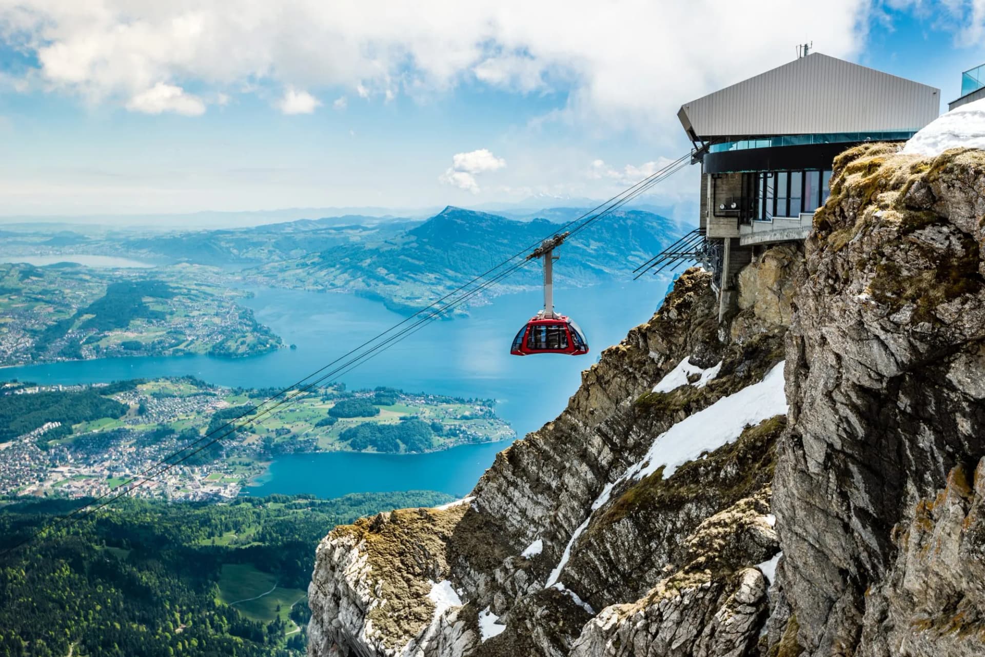 Cable car descending near station above Lake Lucerne with green hills and mountains in Switzerland.