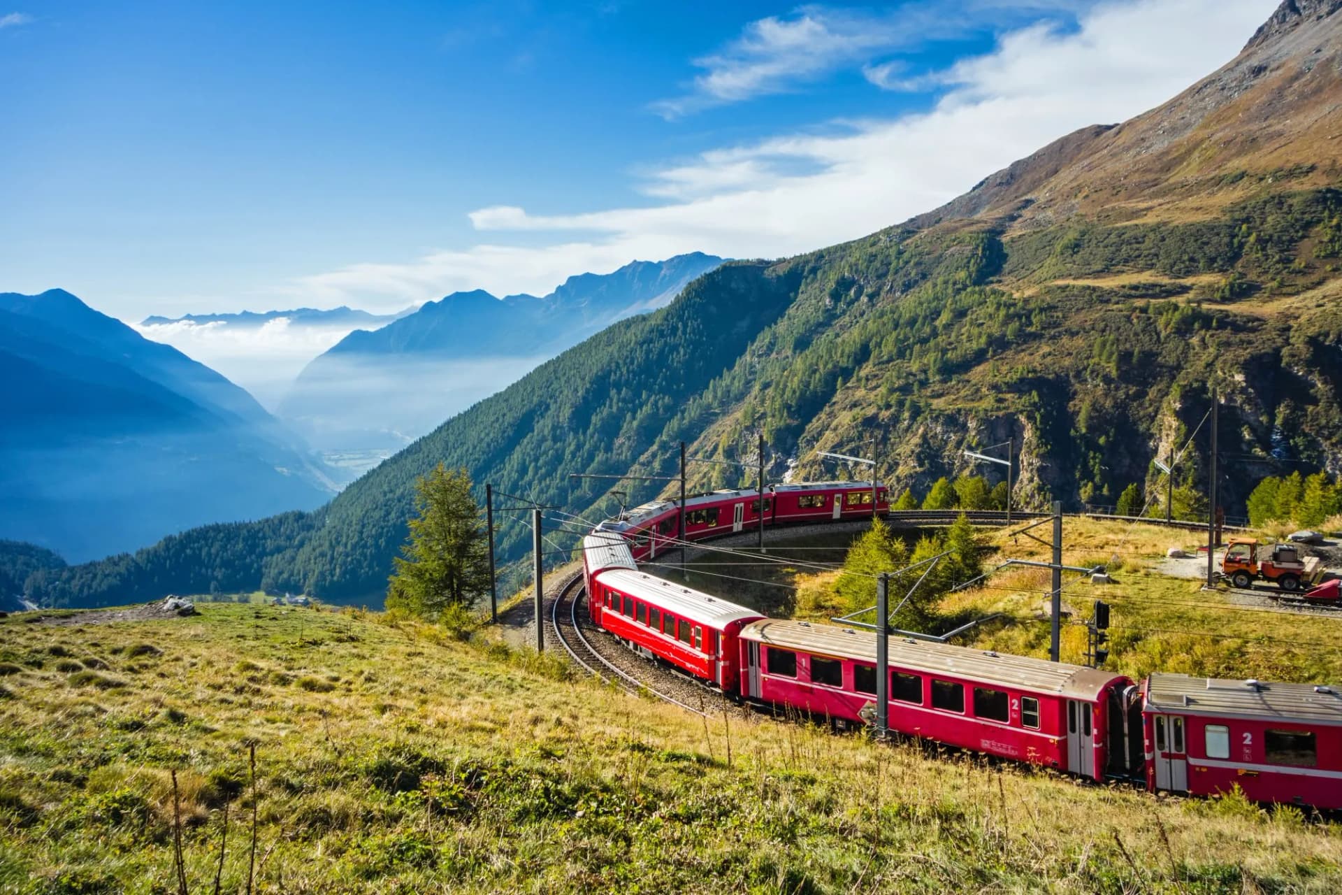 Red train winding through alpine landscape in Graubünden, Switzerland, overlooking a valley.