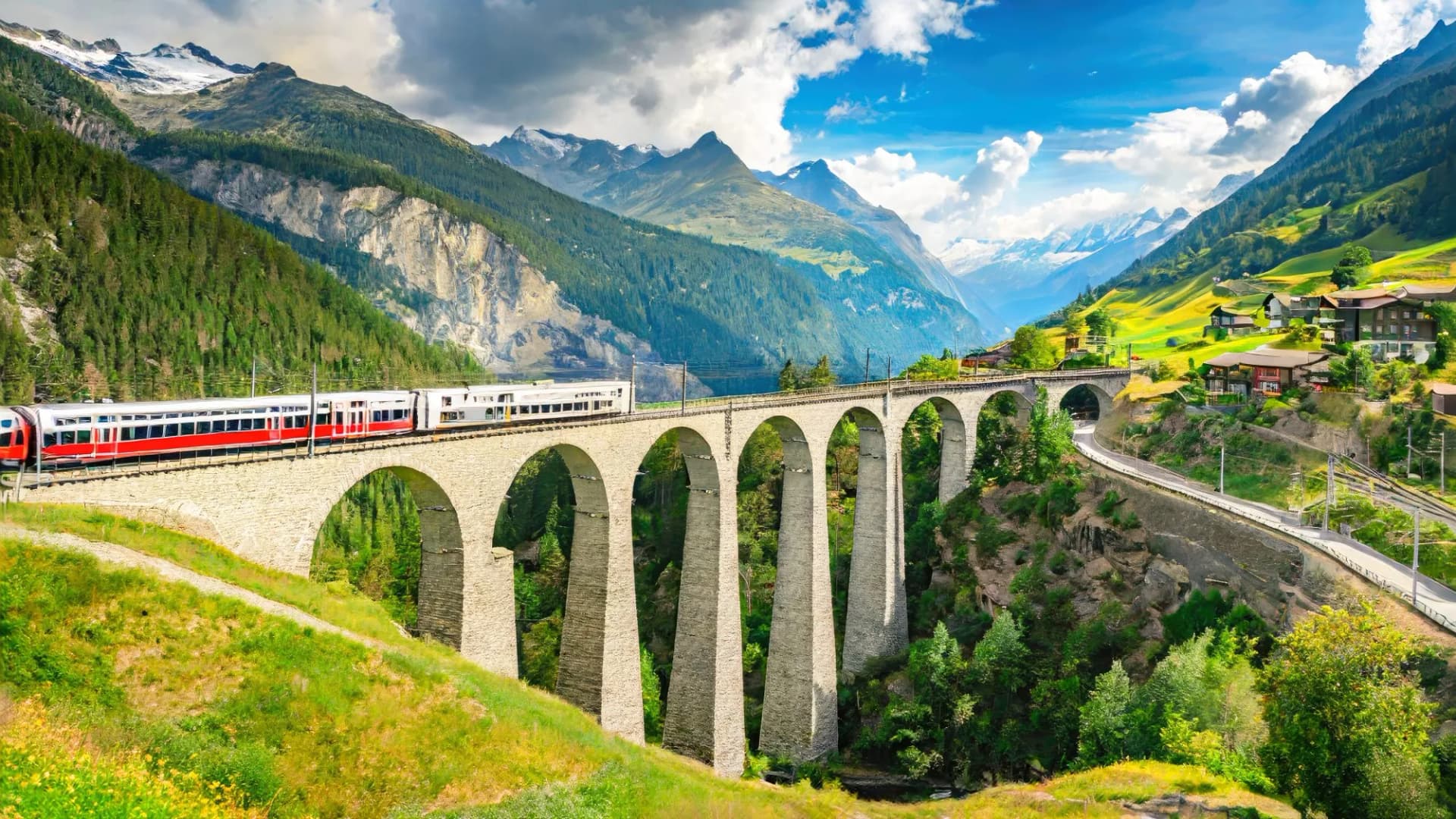 Red train of the Bernina Express on a stone viaduct in the mountains of Switzerland in spring.