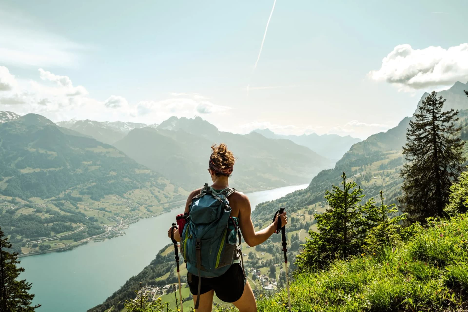 Hiker with backpack and poles enjoys view of Churfirsten mountains and Walensee lake.