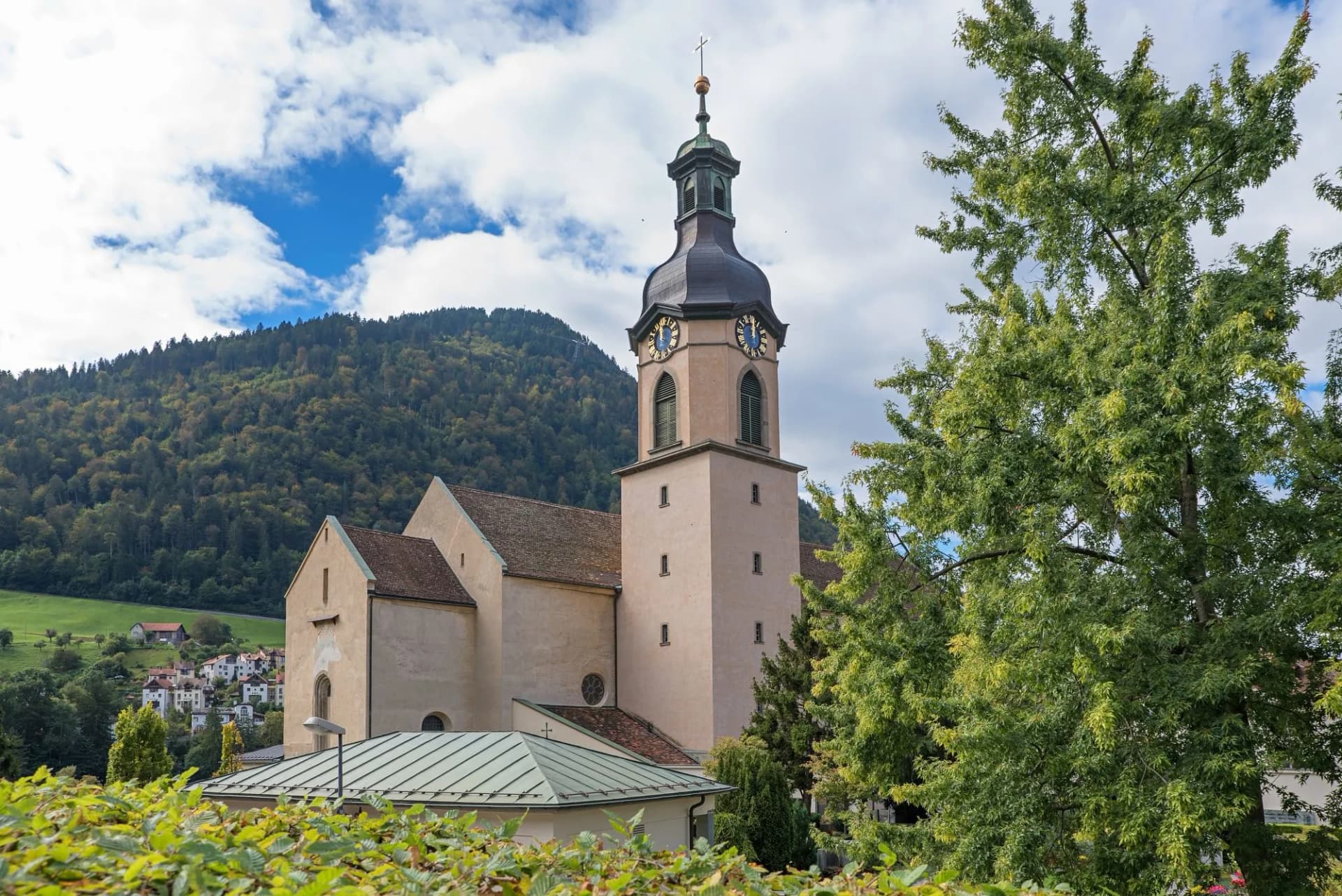 Historic Cathedral of Chur, Switzerland, with clock tower against forested mountain backdrop.