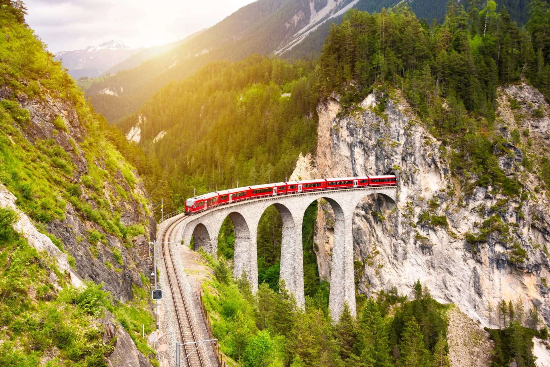 Red Swiss train crossing a high stone viaduct in a lush green mountain valley