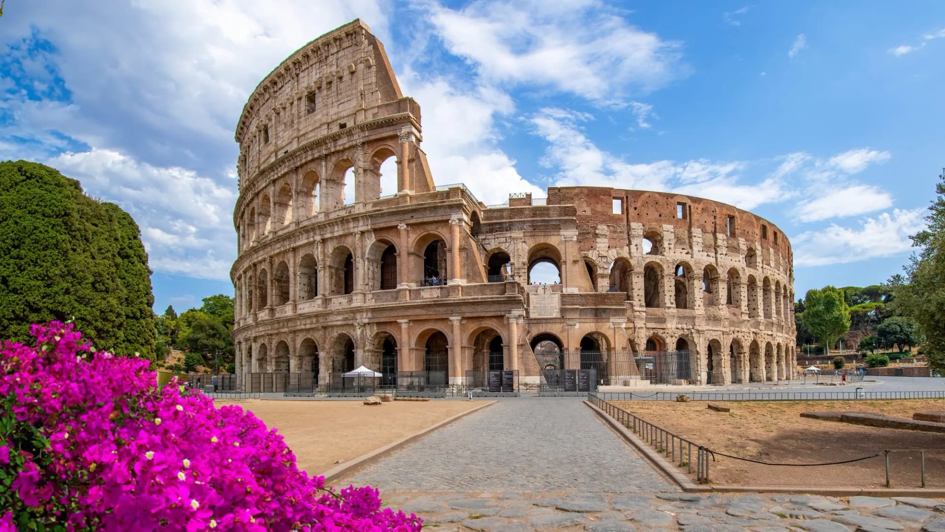 Colosseum in Rome, Italy, with bright pink flowers and blue sky.