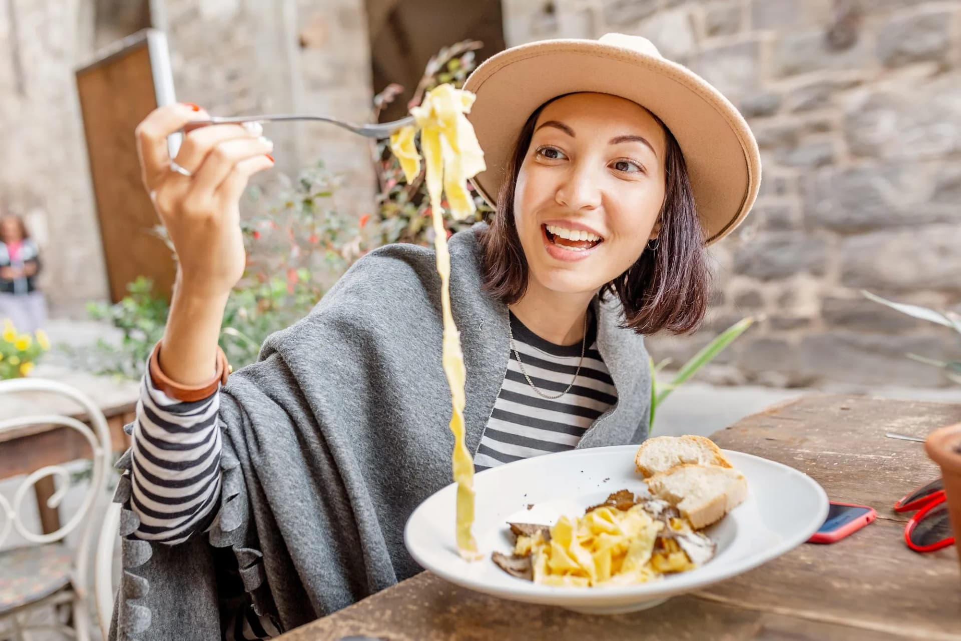 Woman eating truffle pasta with bread outdoors at a stone-walled Italian restaurant